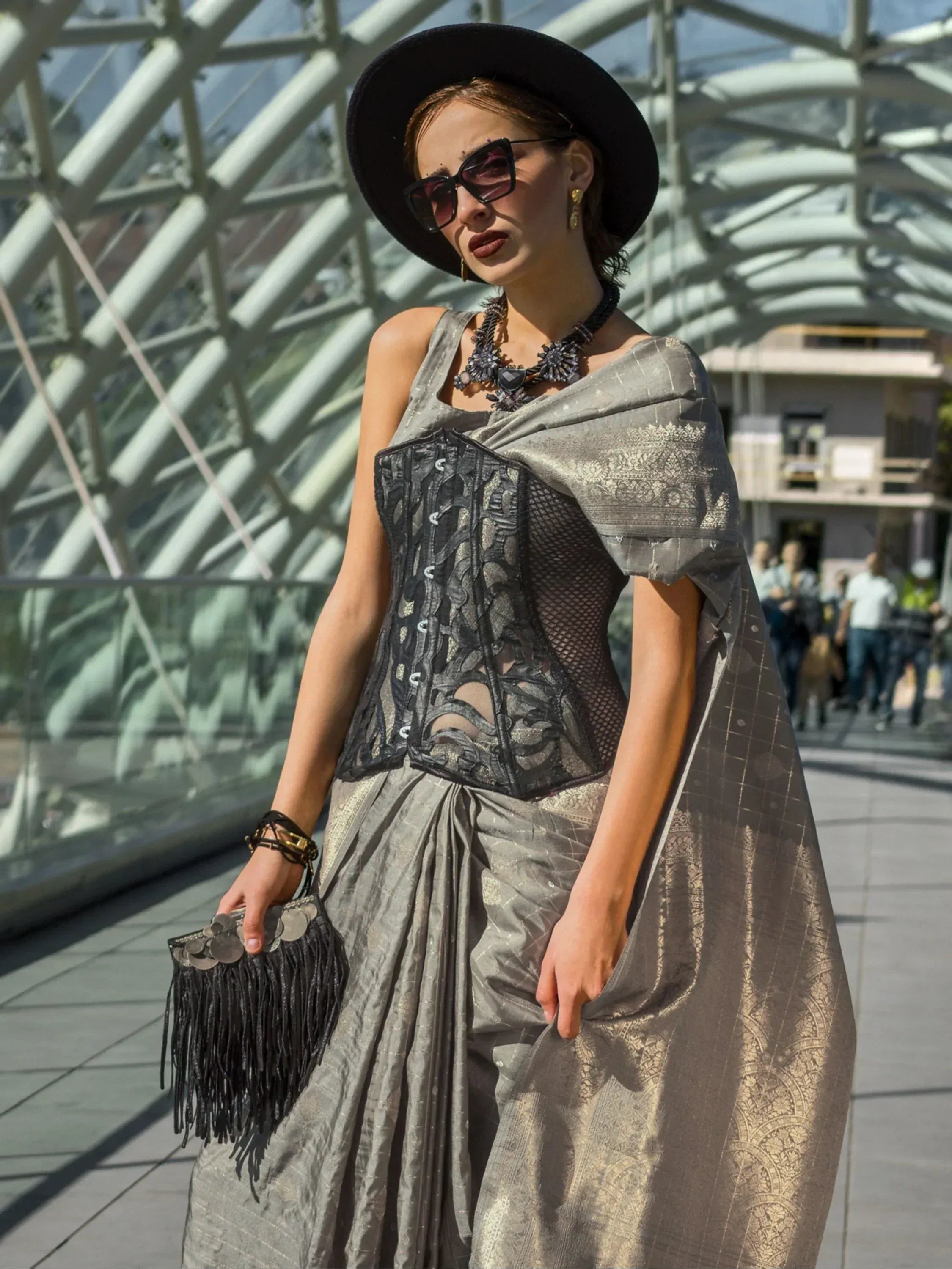 Stylish woman in silver ethnic gown with black corset, hat, and sunglasses, perfect for modern Indian fashion events.