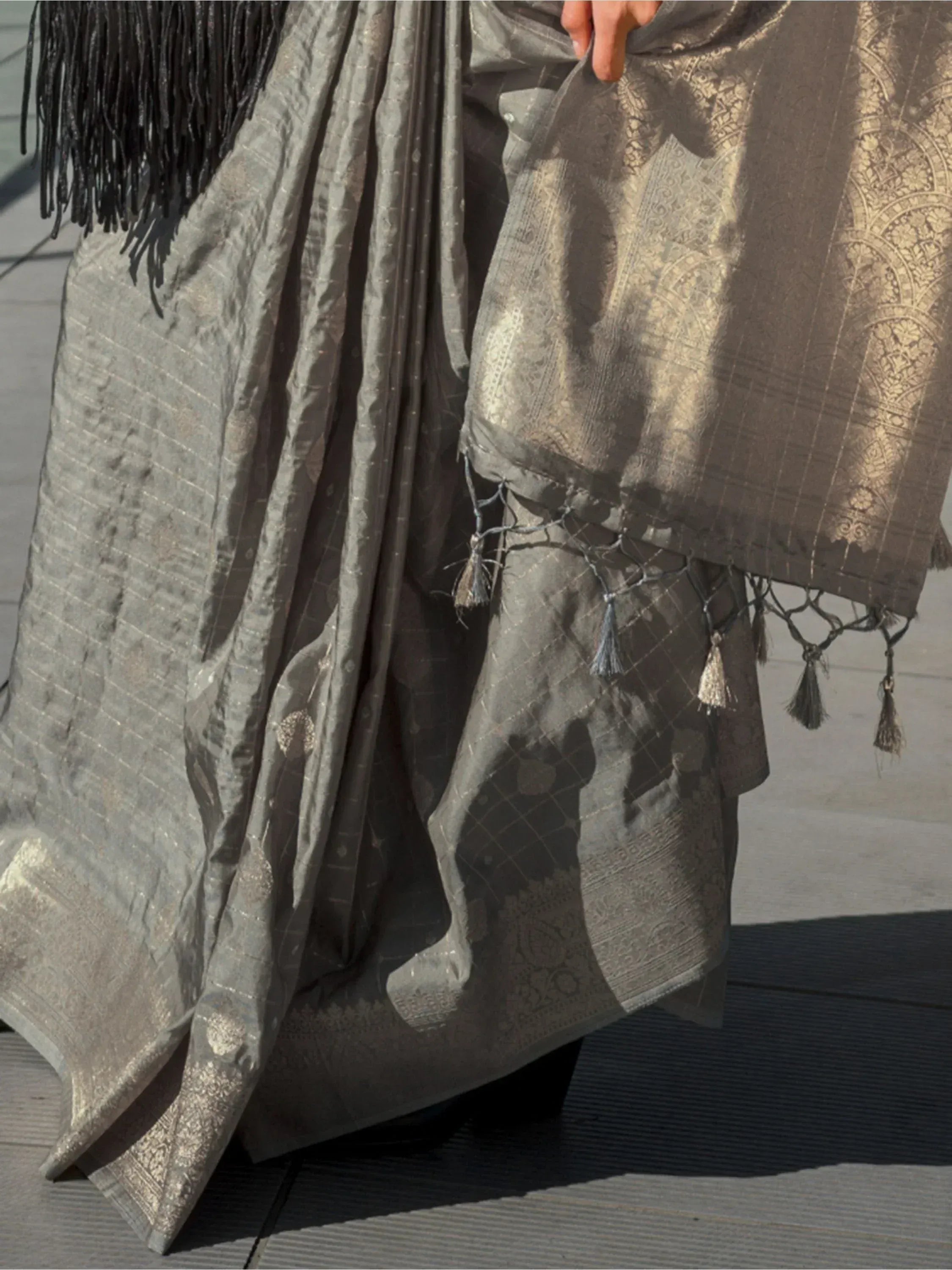 Grey designer saree with gold zari work, tassels, and black fringe detailing for ethnic wear