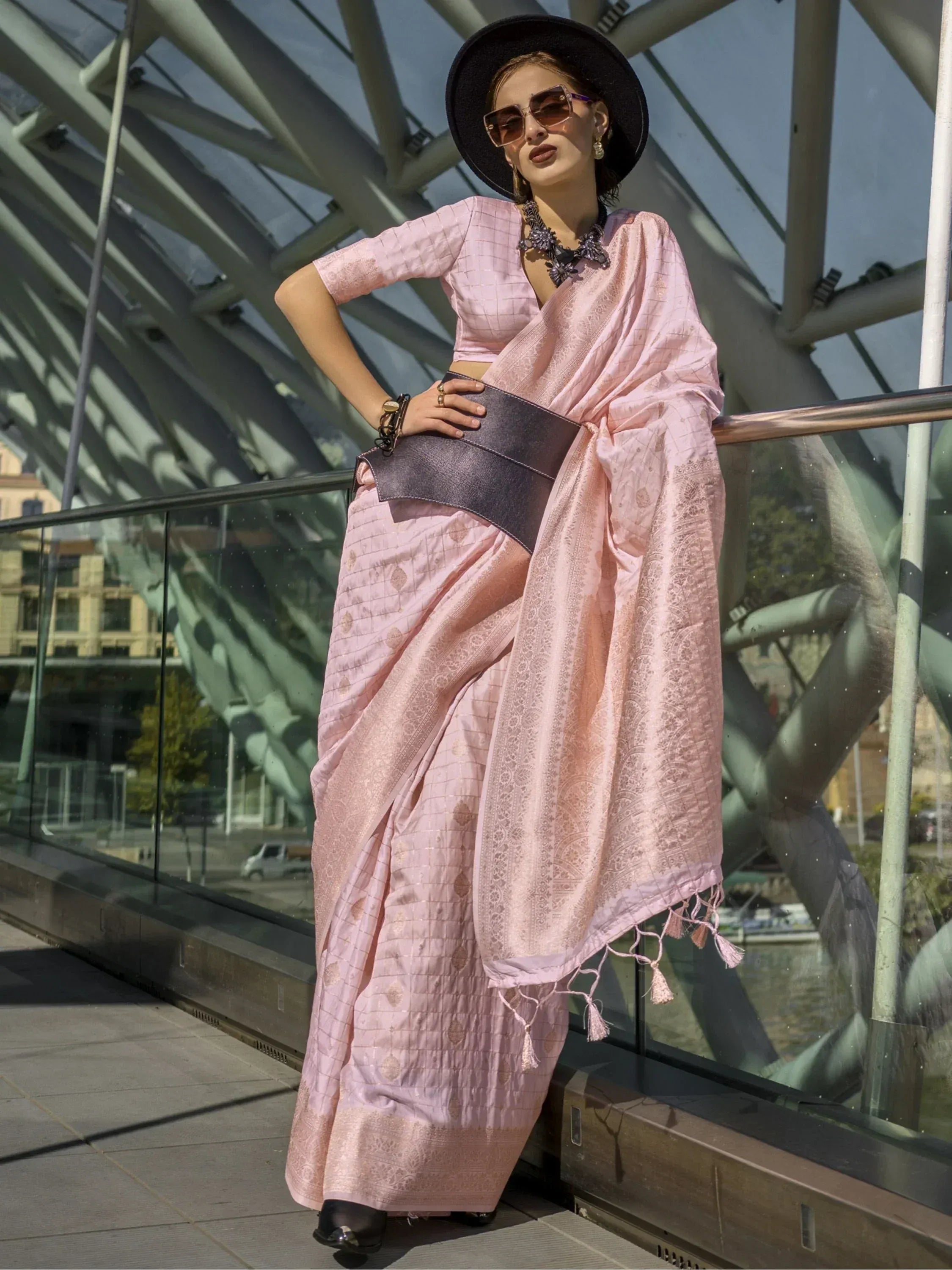 Pink designer saree with checkered pattern and tassels, styled with black hat and belt for modern ethnic look