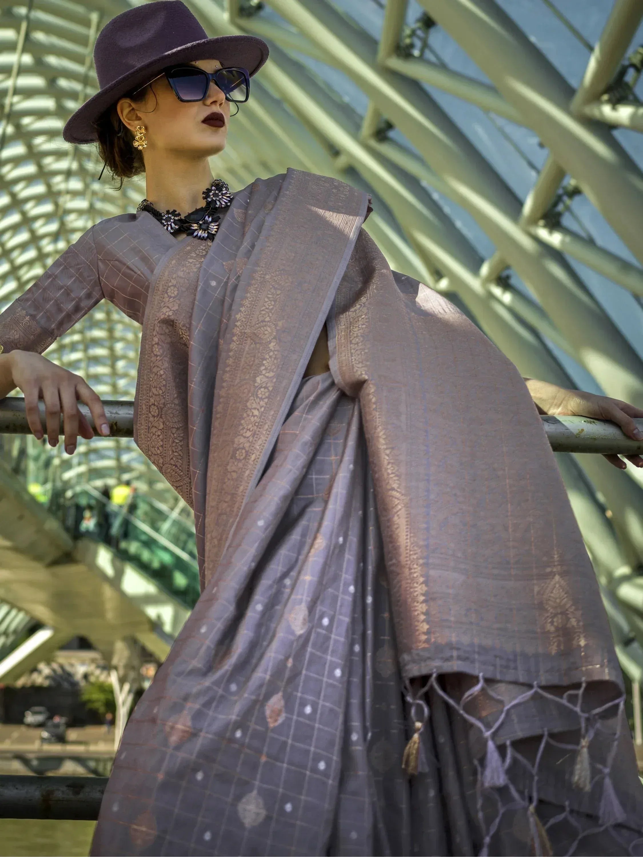 Woman in purple hat wearing elegant Indian saree with gold embroidery and checkered pattern, styled with statement jewelry.