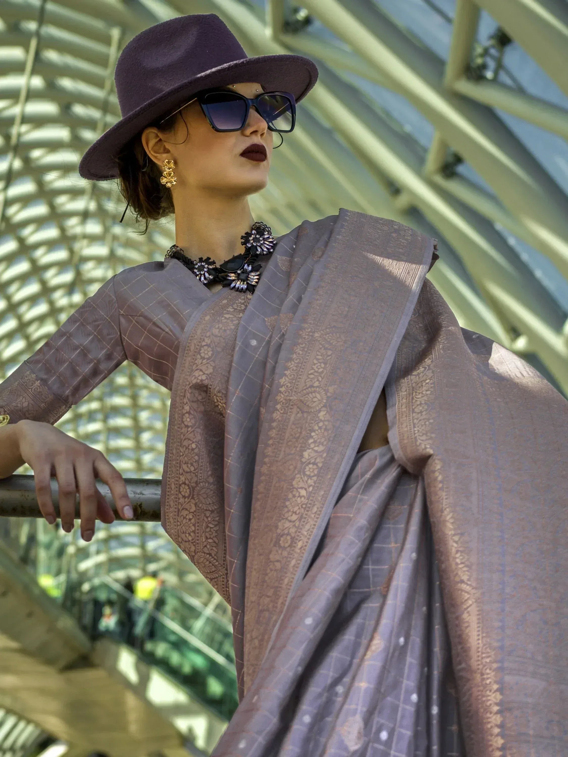 Woman in purple hat and sunglasses wearing elegant ethnic saree with gold embroidery, modern Indian fashion