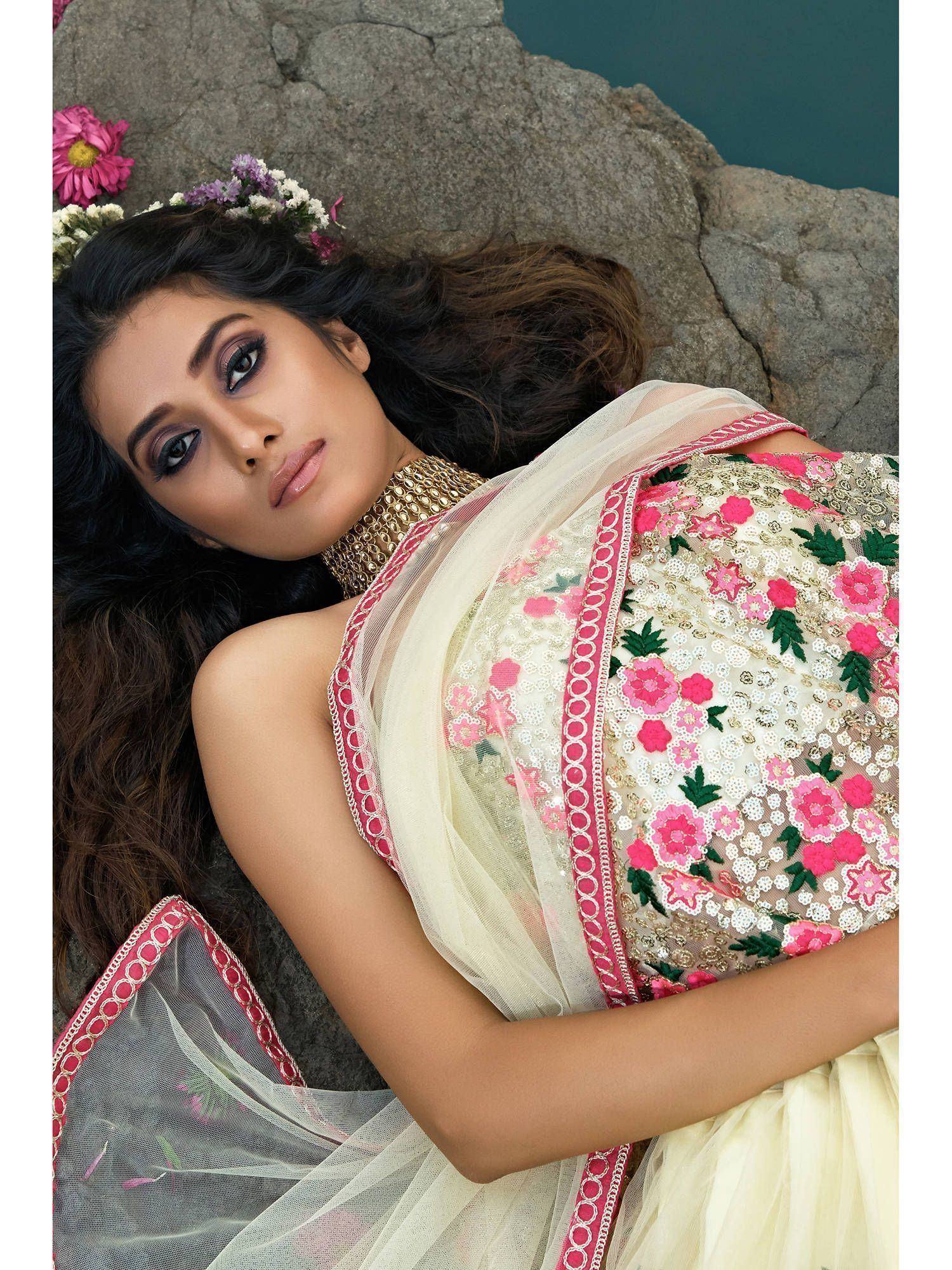 Woman in floral embroidered ethnic gown with pink detailing, lying on rocks near water