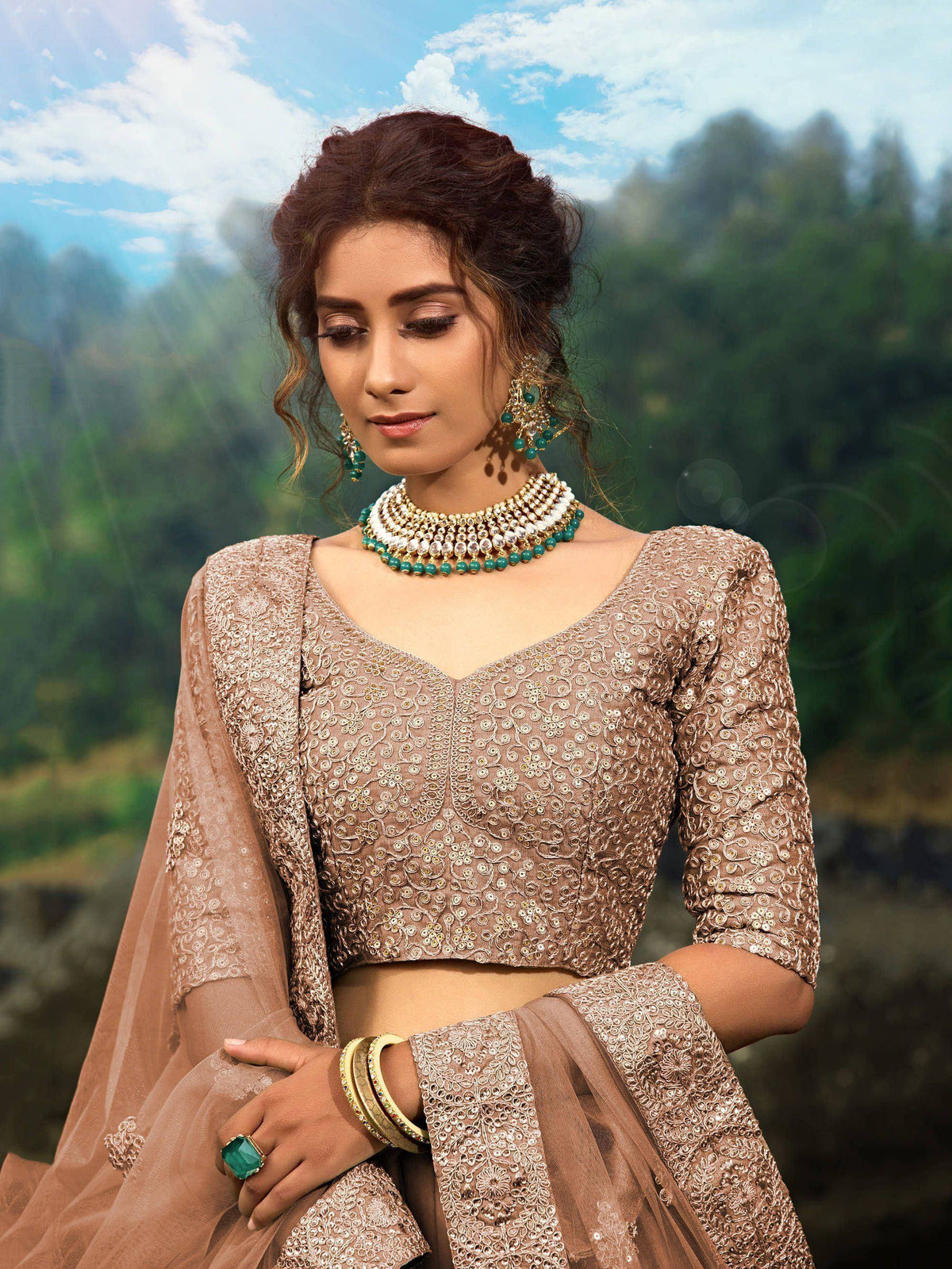 Elegant beige embroidered lehenga choli with green jewelry, perfect for Indian ethnic wear occasions.