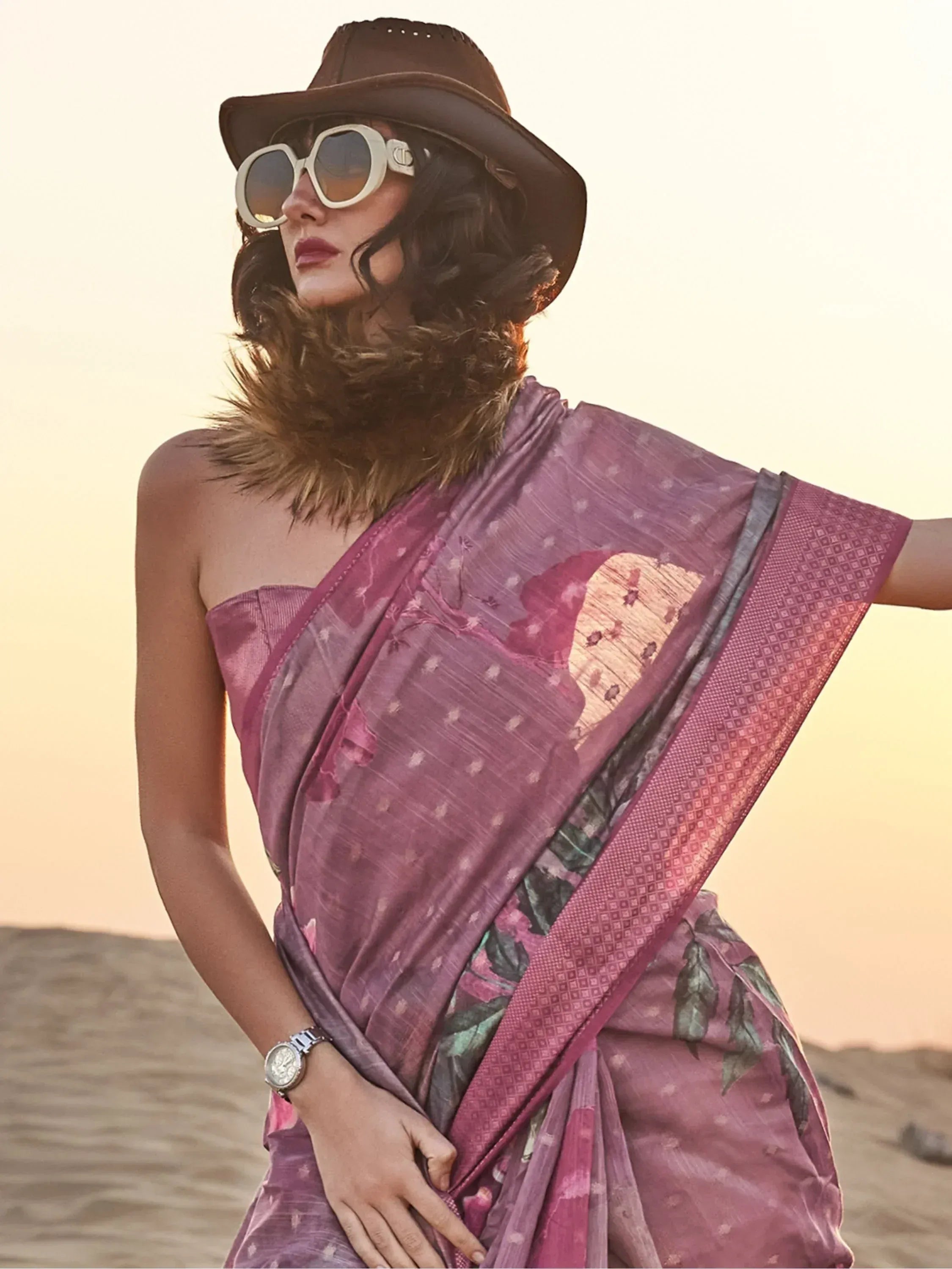 Woman in purple floral saree with hat and sunglasses, desert sunset backdrop, ethnic fashion
