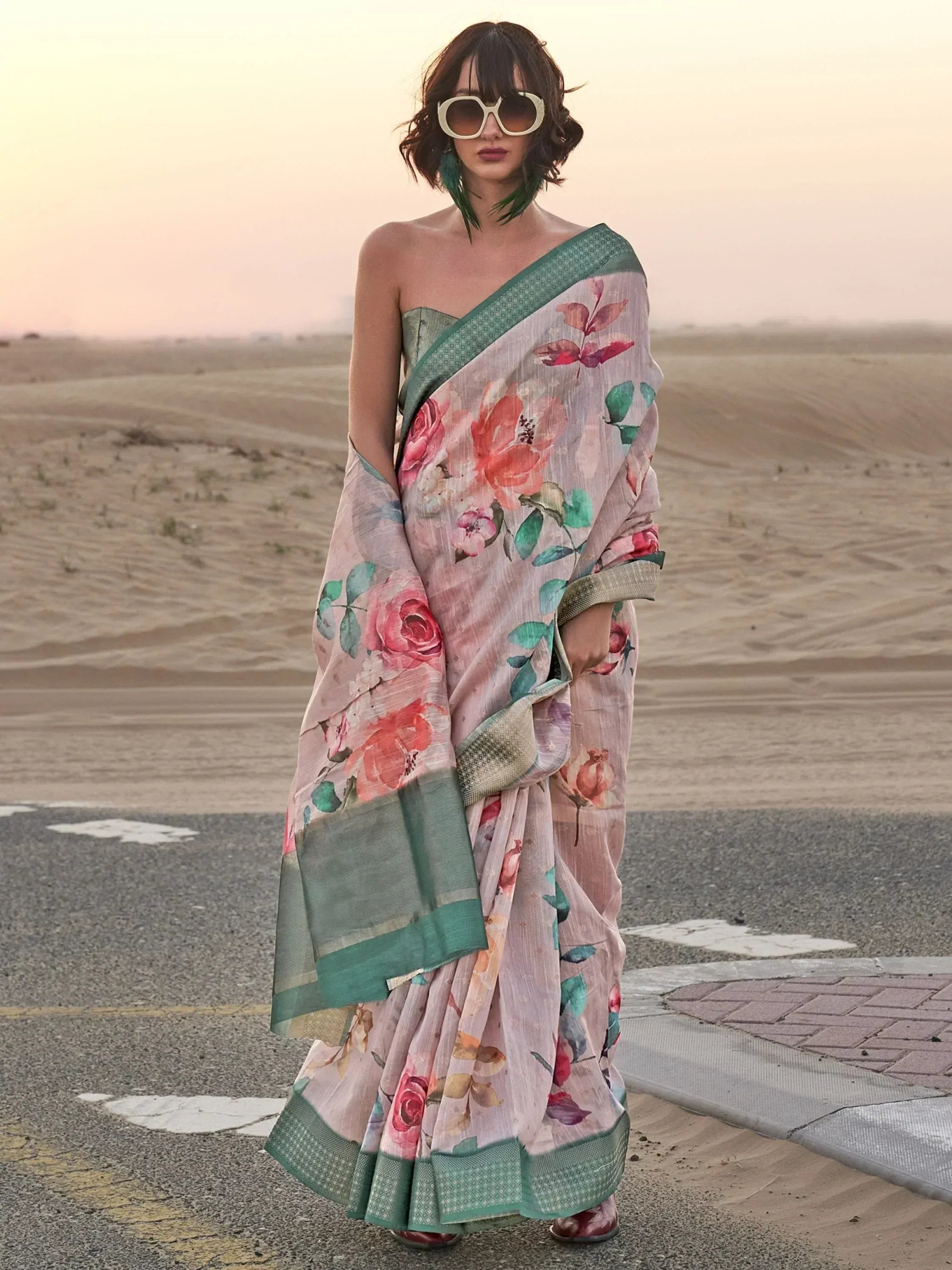 Woman in floral print saree with green border, styled for ethnic wear, standing in desert at sunset