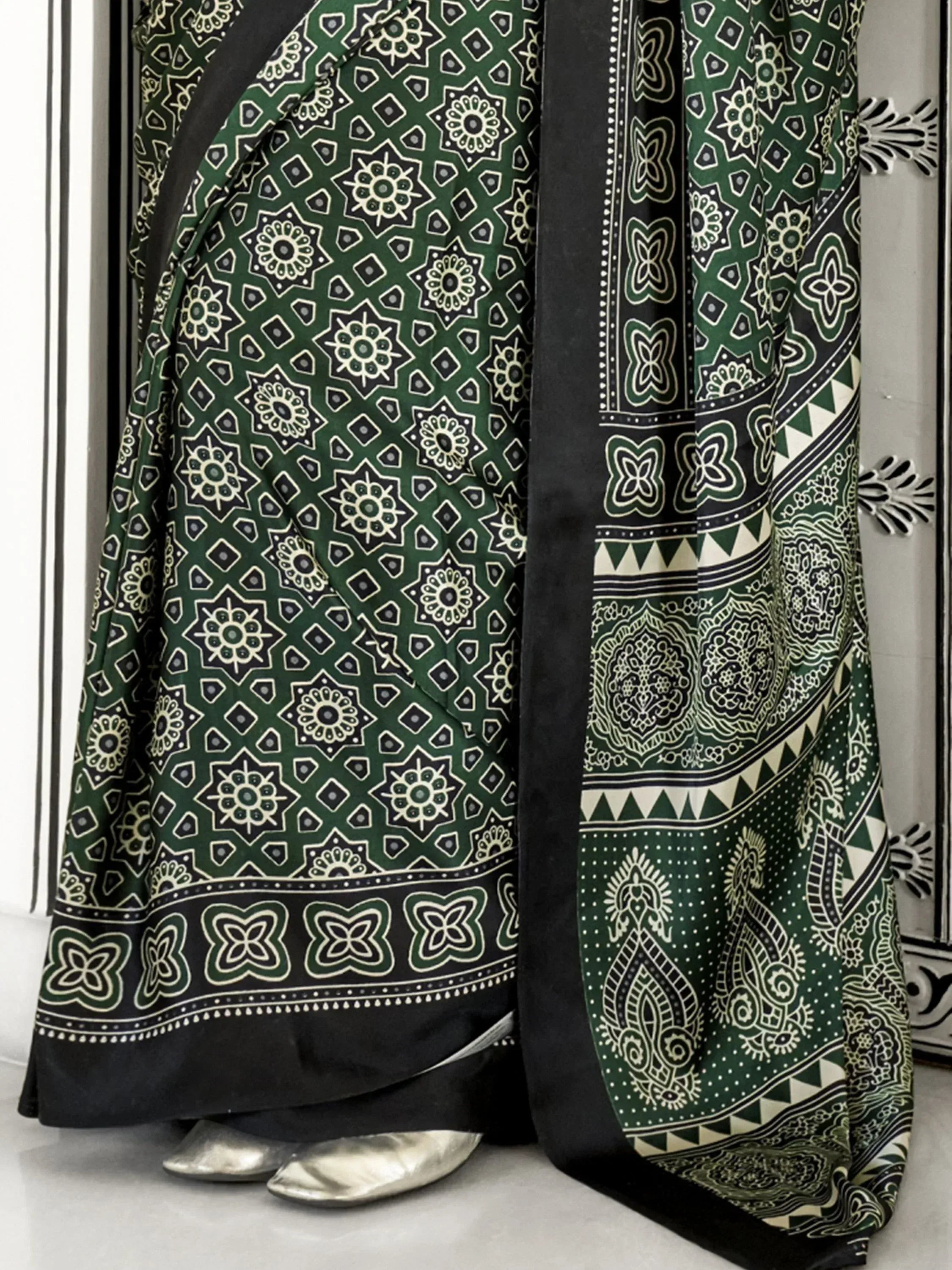 Green and black printed saree with geometric and floral motifs, paired with silver heels for ethnic wear.