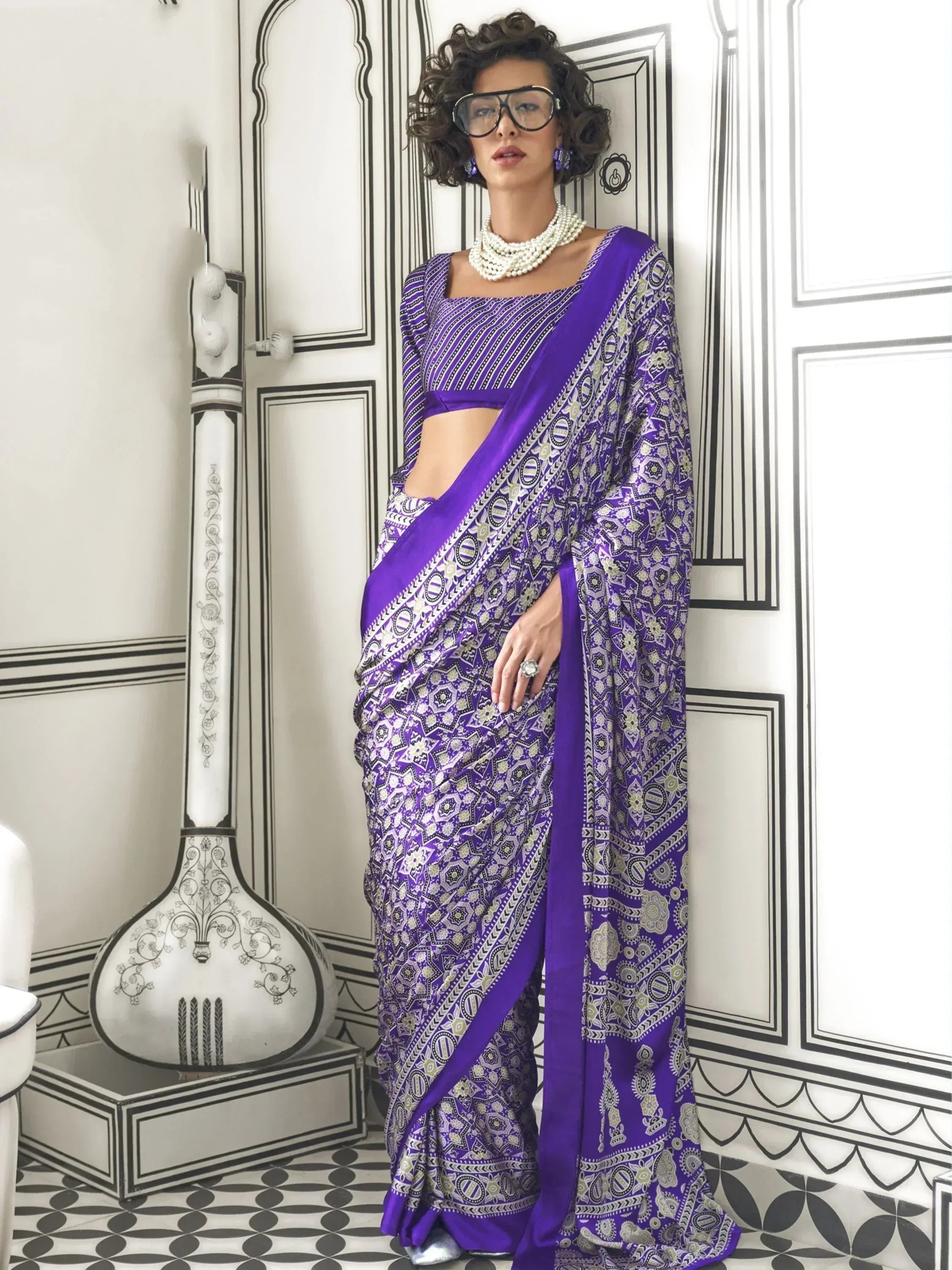 Purple printed saree with geometric patterns, paired with matching blouse and pearl necklace, styled for ethnic wear.