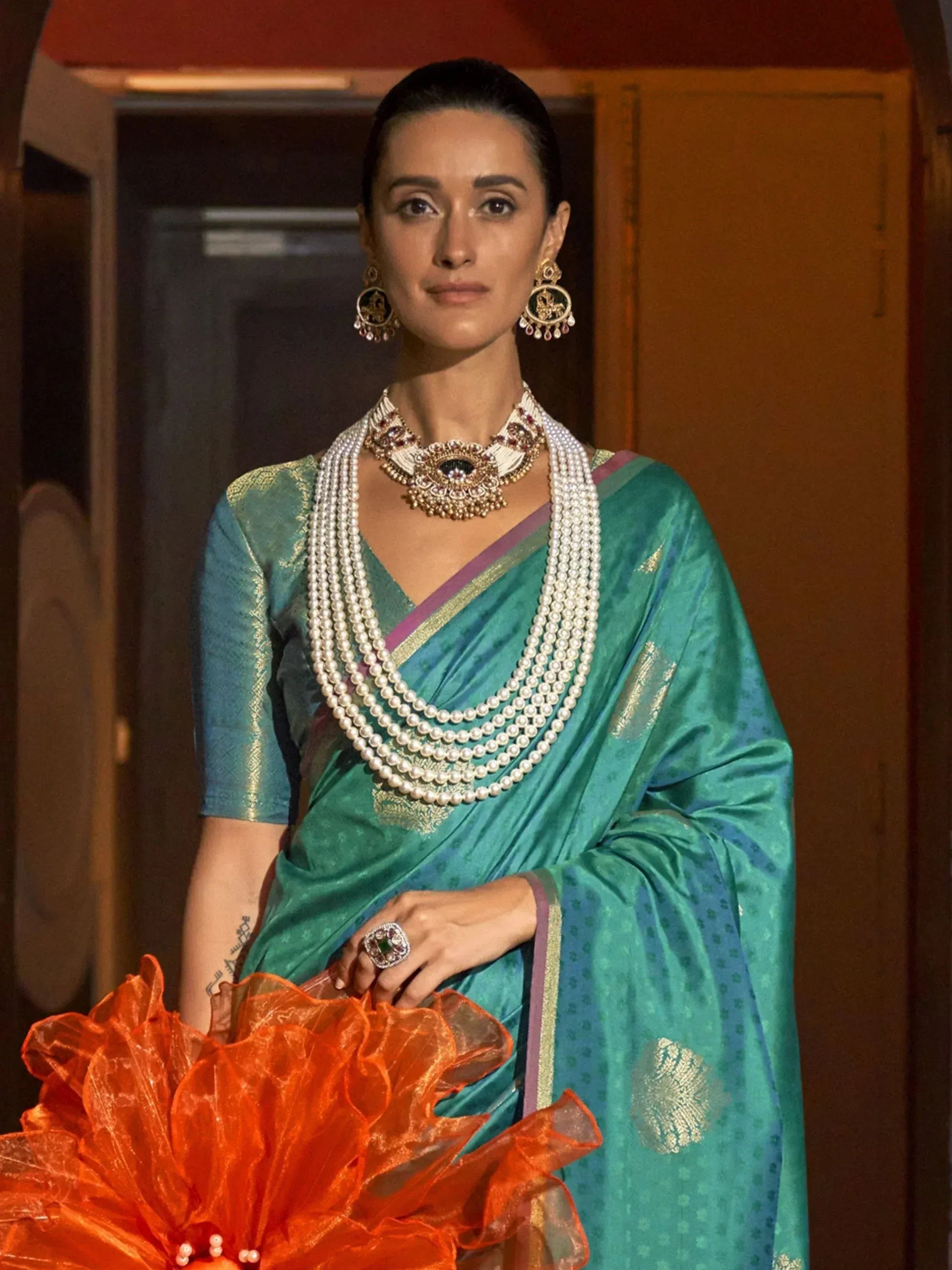 Woman in teal designer saree with gold embroidery, pearl necklace, and traditional Indian jewelry