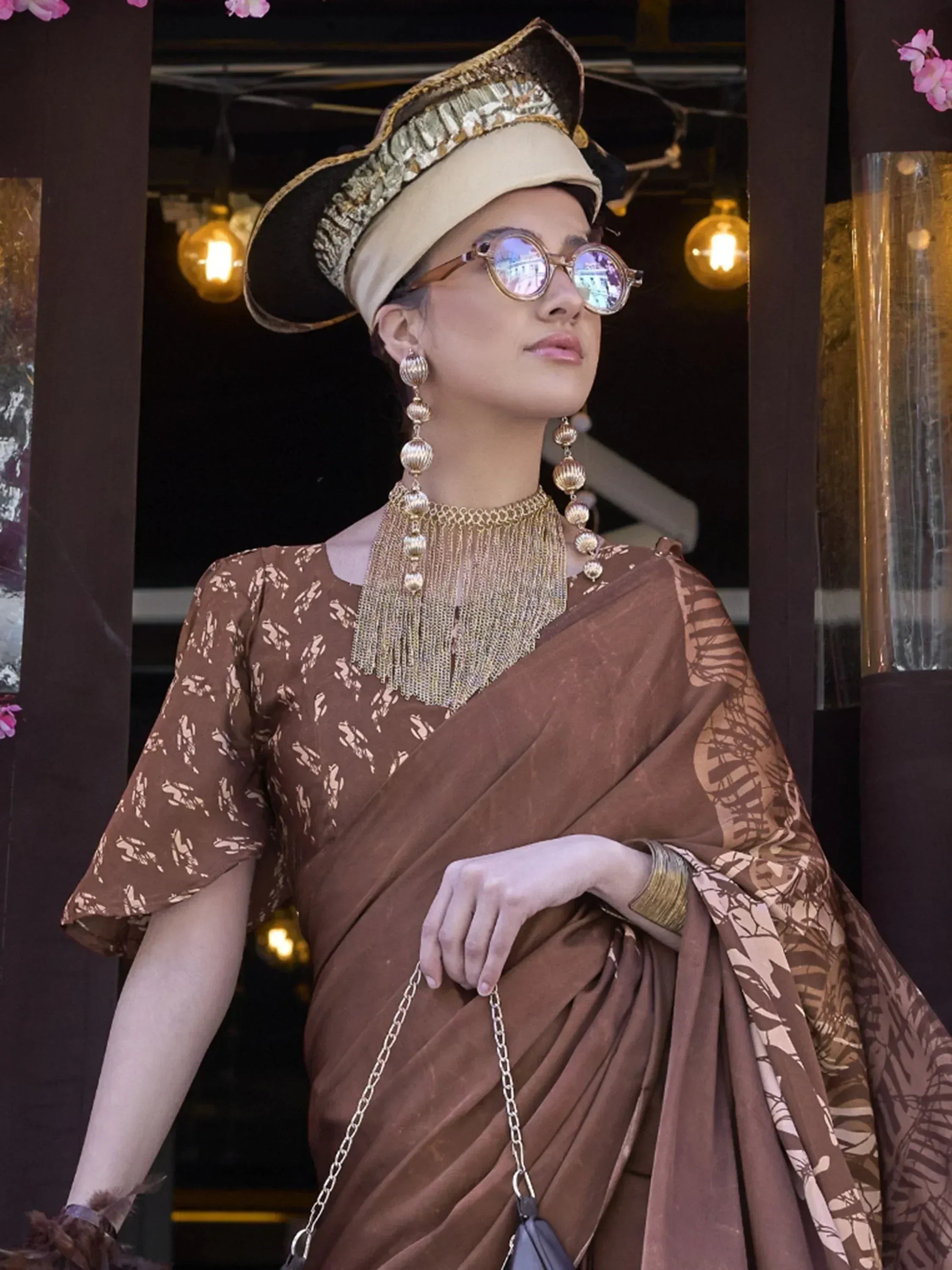 Woman in brown printed saree with gold jewelry and stylish hat, ethnic fashion
