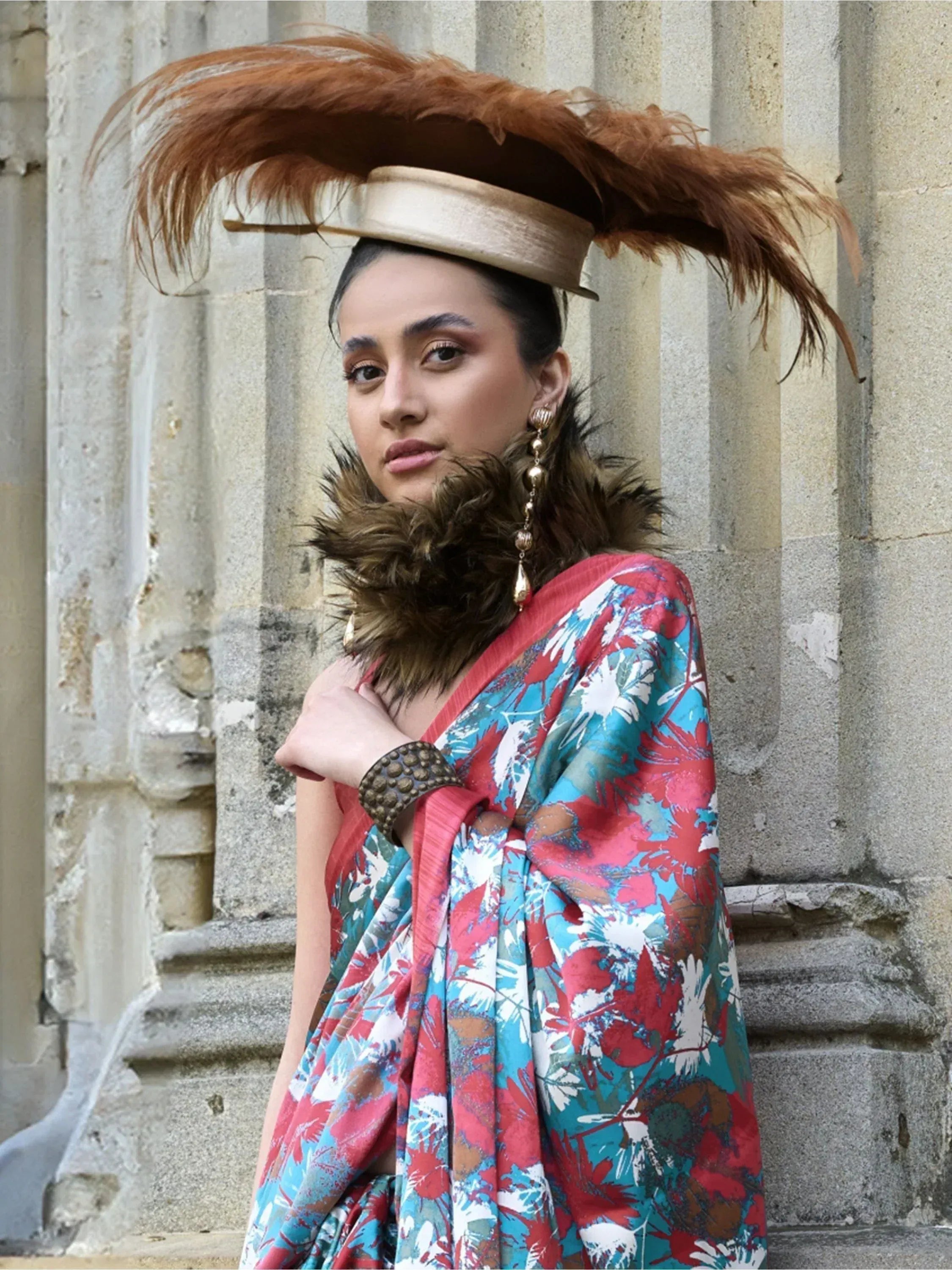 Woman in vibrant floral ethnic gown with feathered hat and fur collar, perfect for festive occasions.