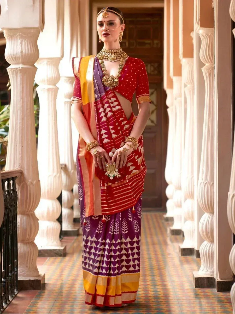 Woman in vibrant red and purple ethnic saree with gold jewelry, standing in traditional Indian corridor