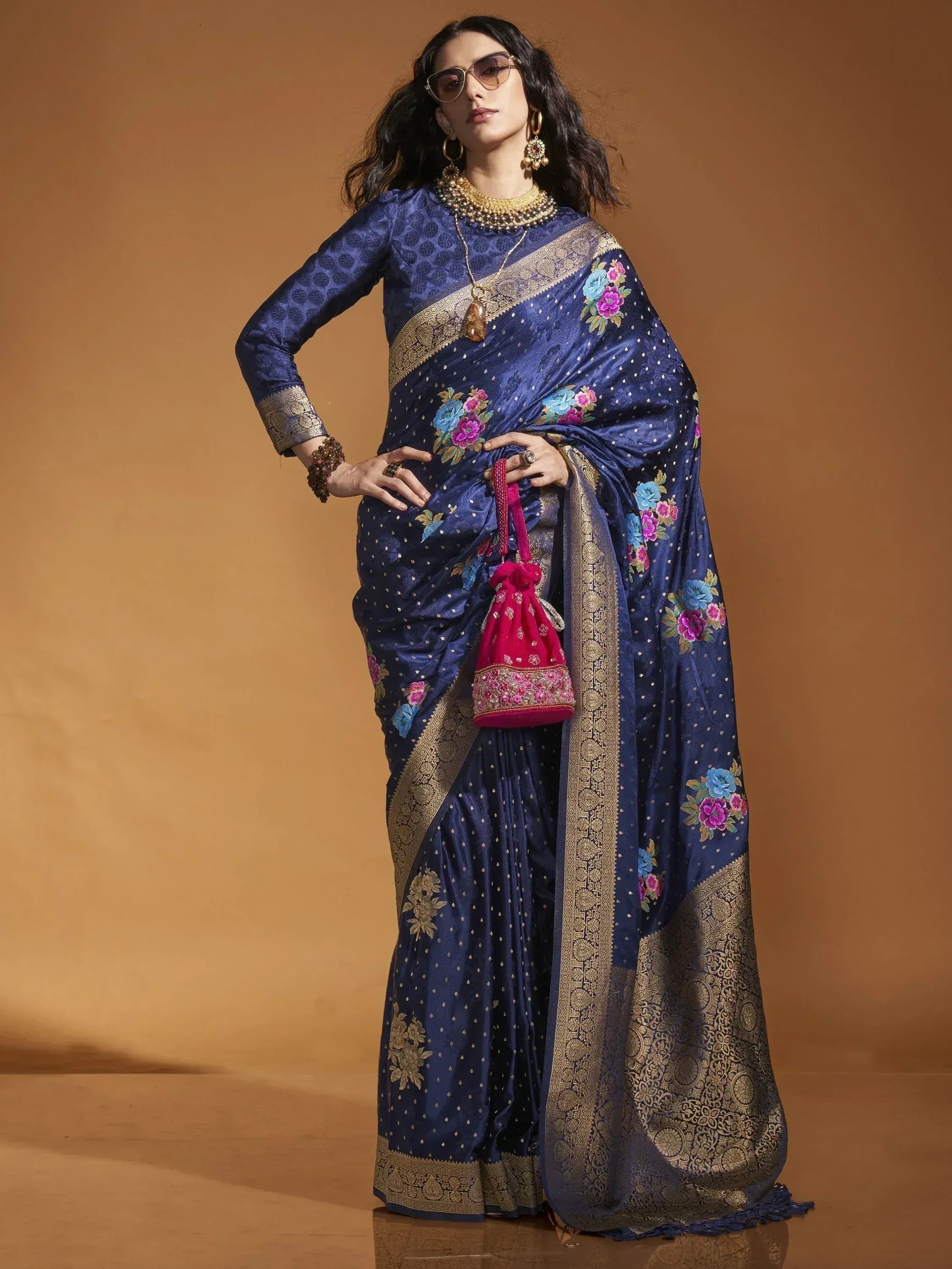 Navy blue embroidered saree with gold border and floral motifs, paired with matching blouse and pink potli bag