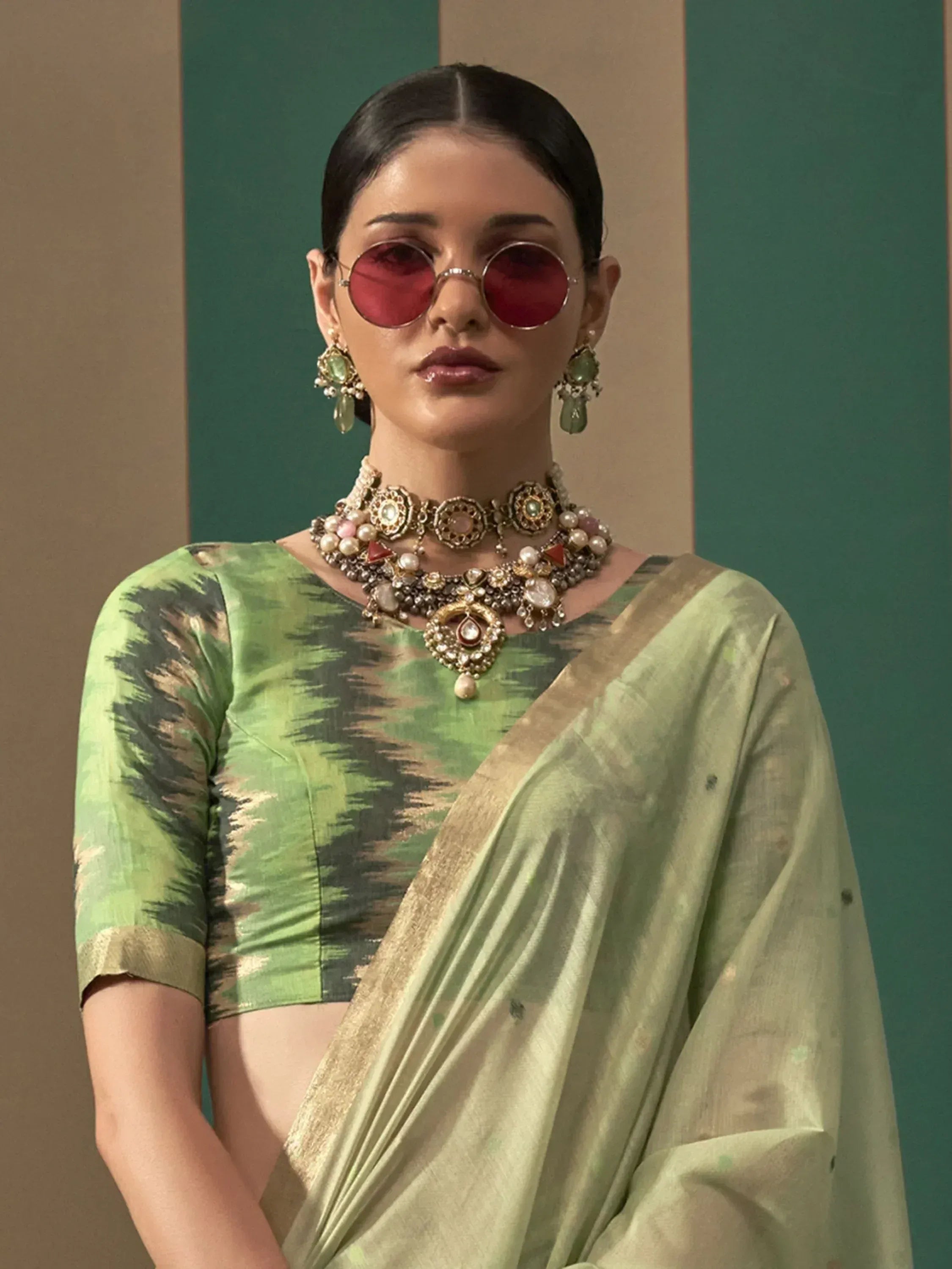 Woman in green ikat saree with gold border, statement jewelry, and red sunglasses