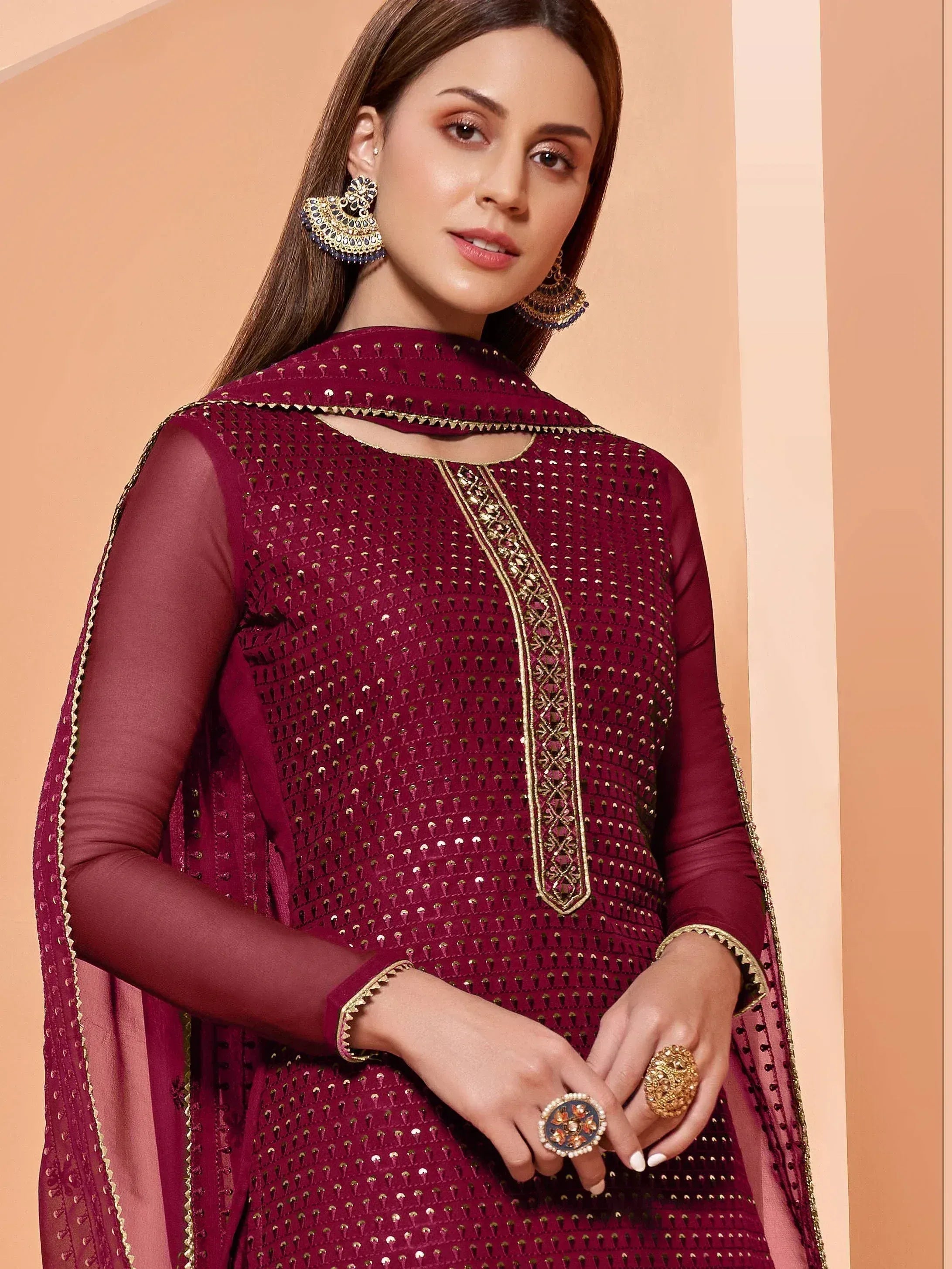 Maroon ethnic wear with gold embroidery, sheer sleeves, and statement jewelry for festive occasions