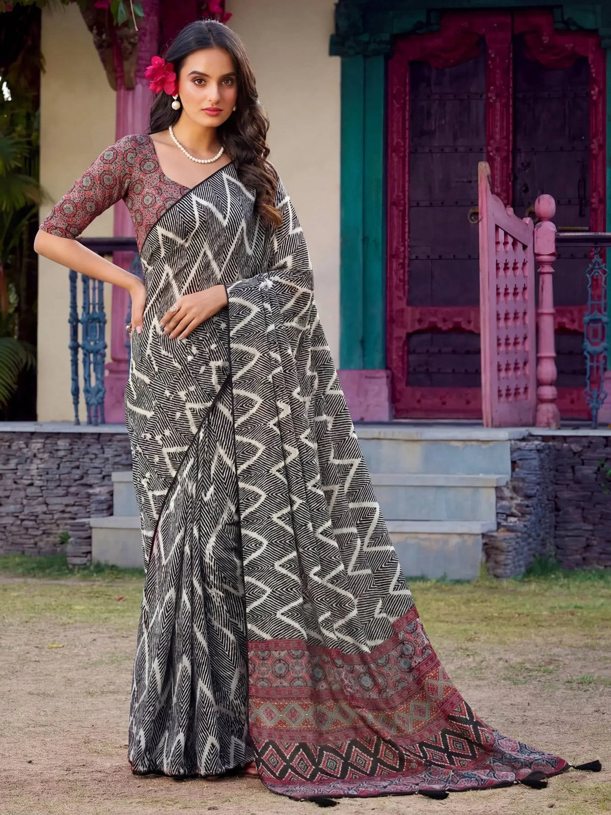 Woman in black and white geometric print saree with red border, styled with pearl necklace and floral hair accessory