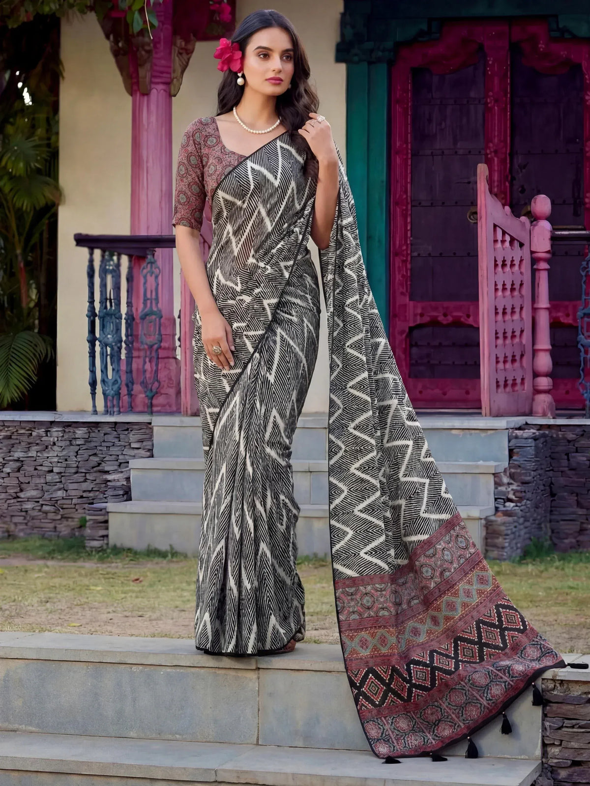 Woman in black and white geometric print saree with colorful border, styled with floral hair accessory and pearl necklace