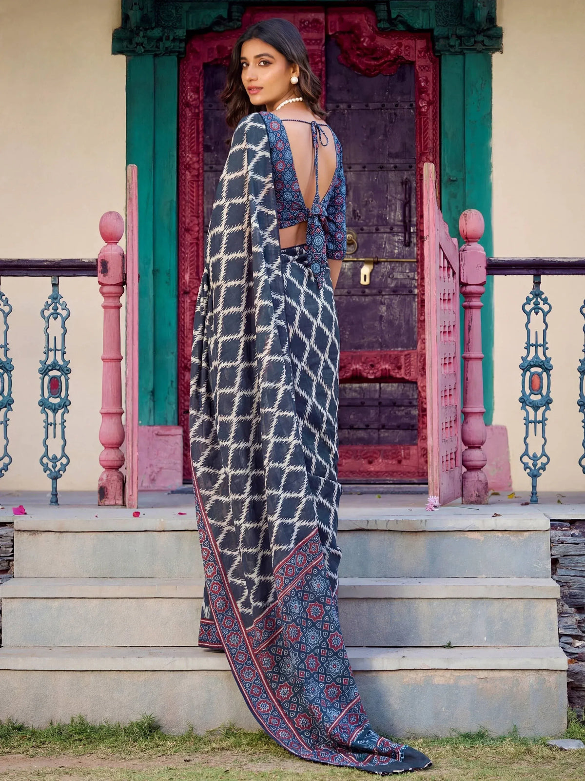 Woman in blue and white ikat print saree with floral border, standing on steps near colorful door