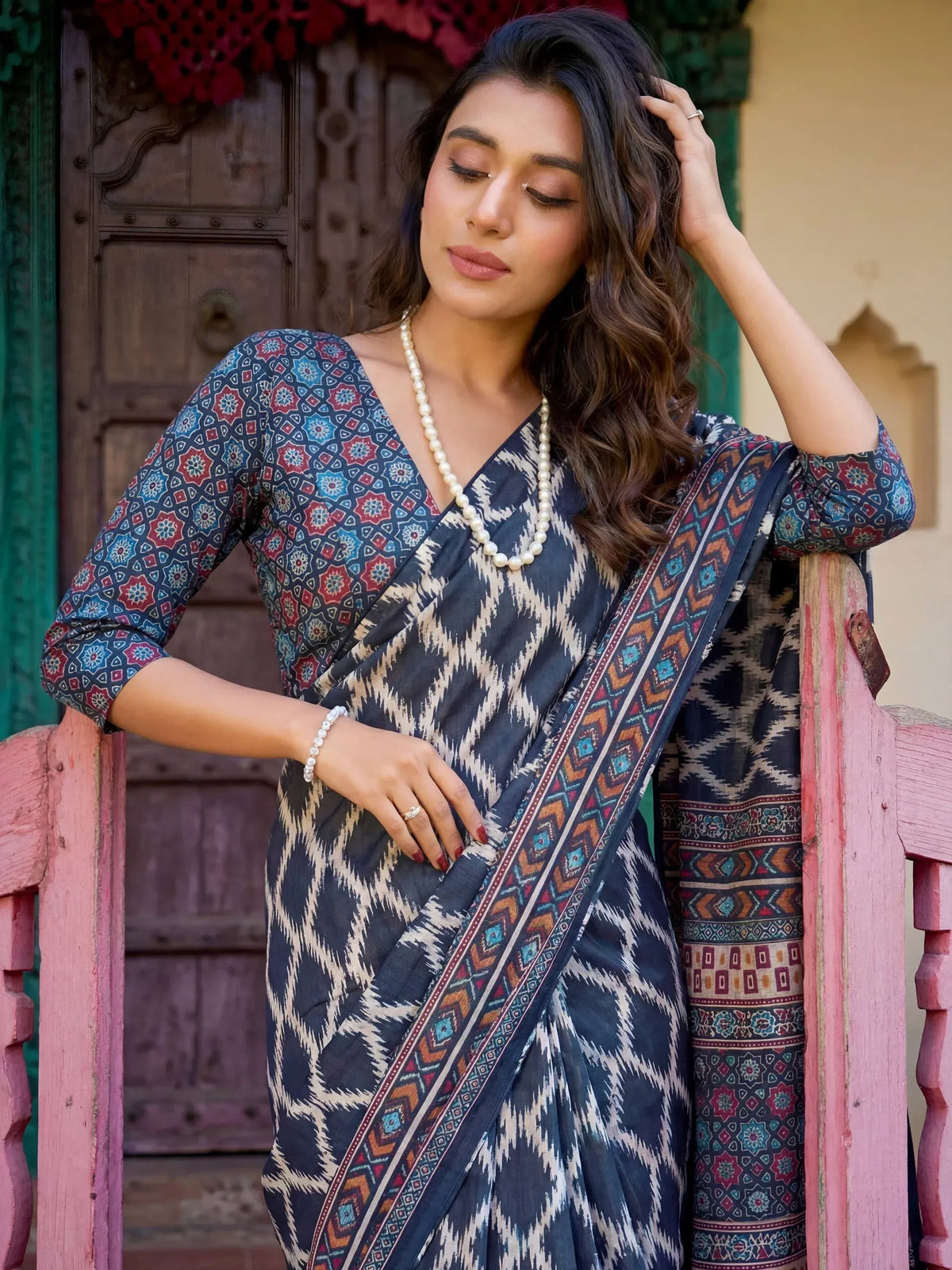 Woman in elegant blue and white ikat print saree with geometric border, styled with pearl necklace for ethnic wear