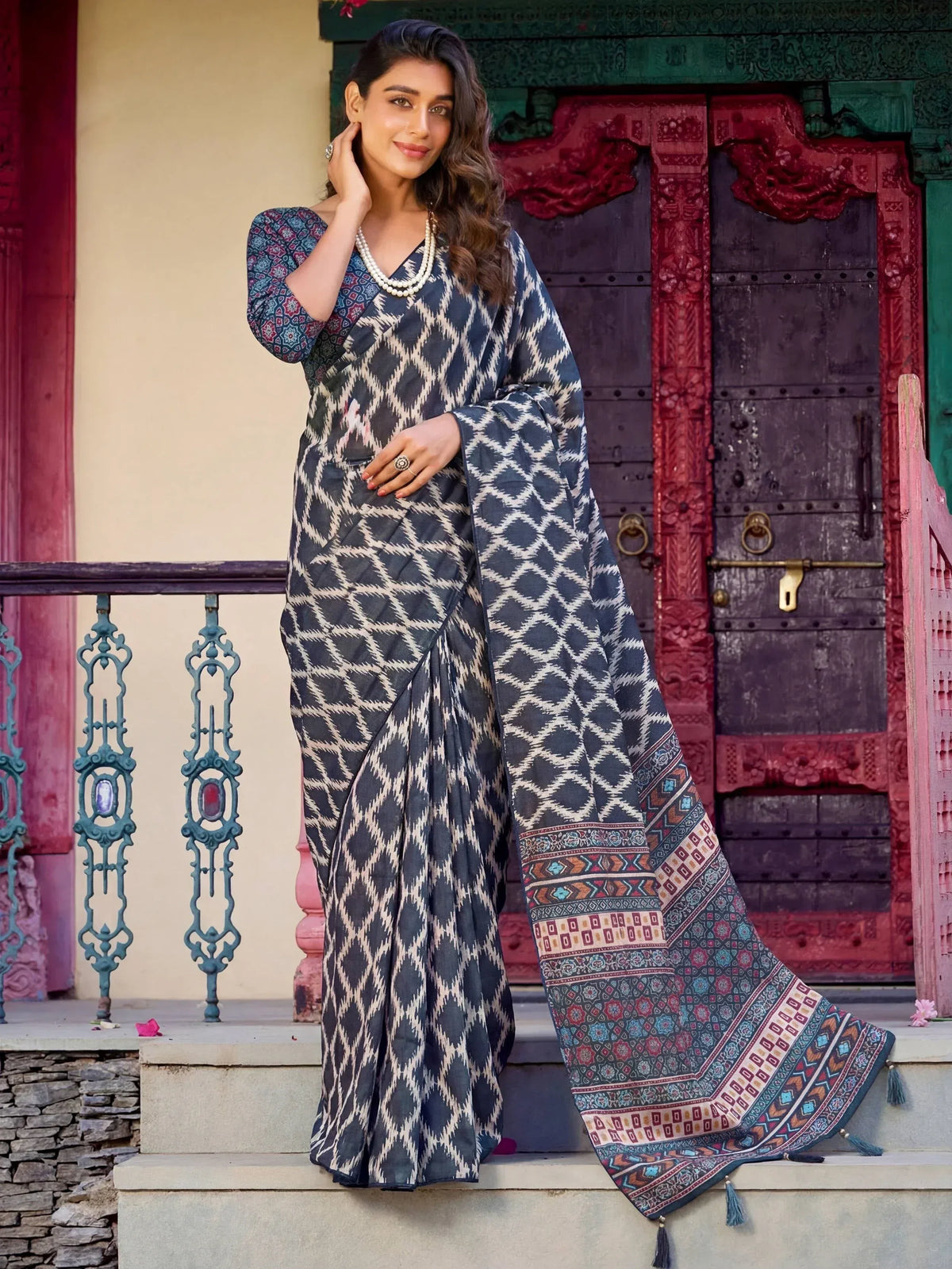 Woman in elegant blue and white ikat print saree with colorful border, styled with pearl necklace, perfect for ethnic occasions.