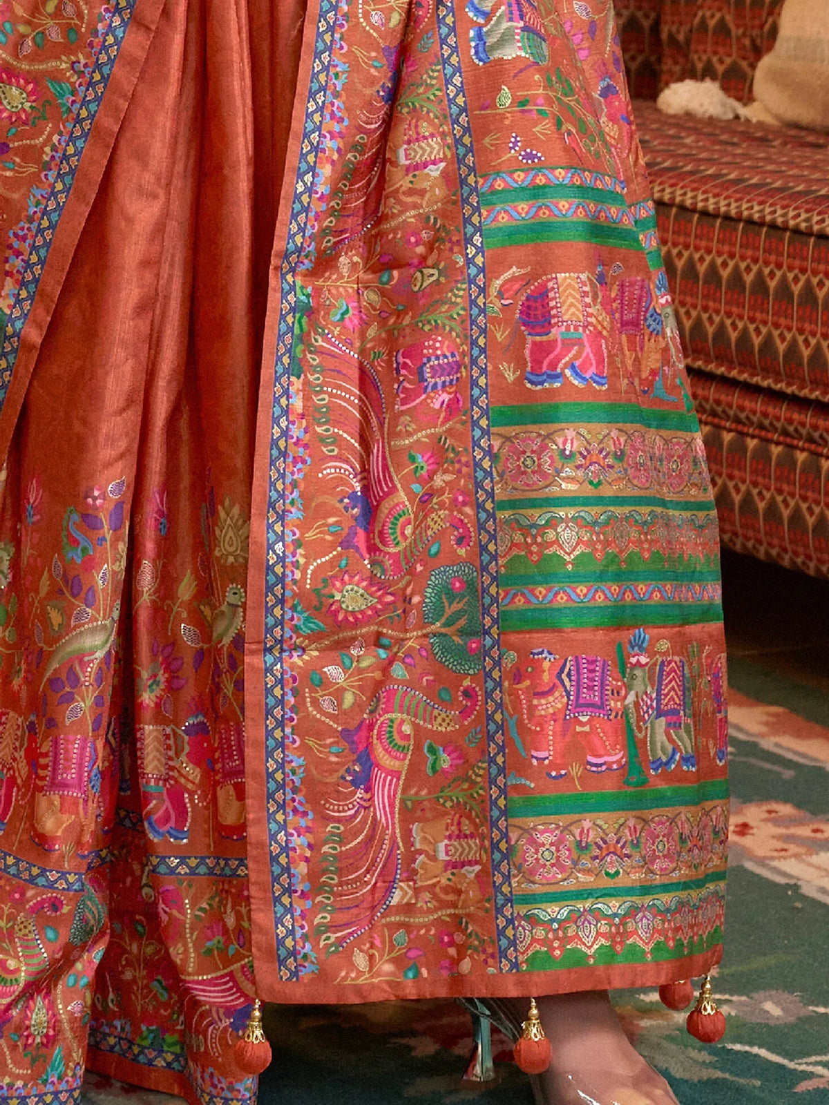 Vibrant orange Indian lehenga with elephant and peacock embroidery, colorful borders, and tassels.