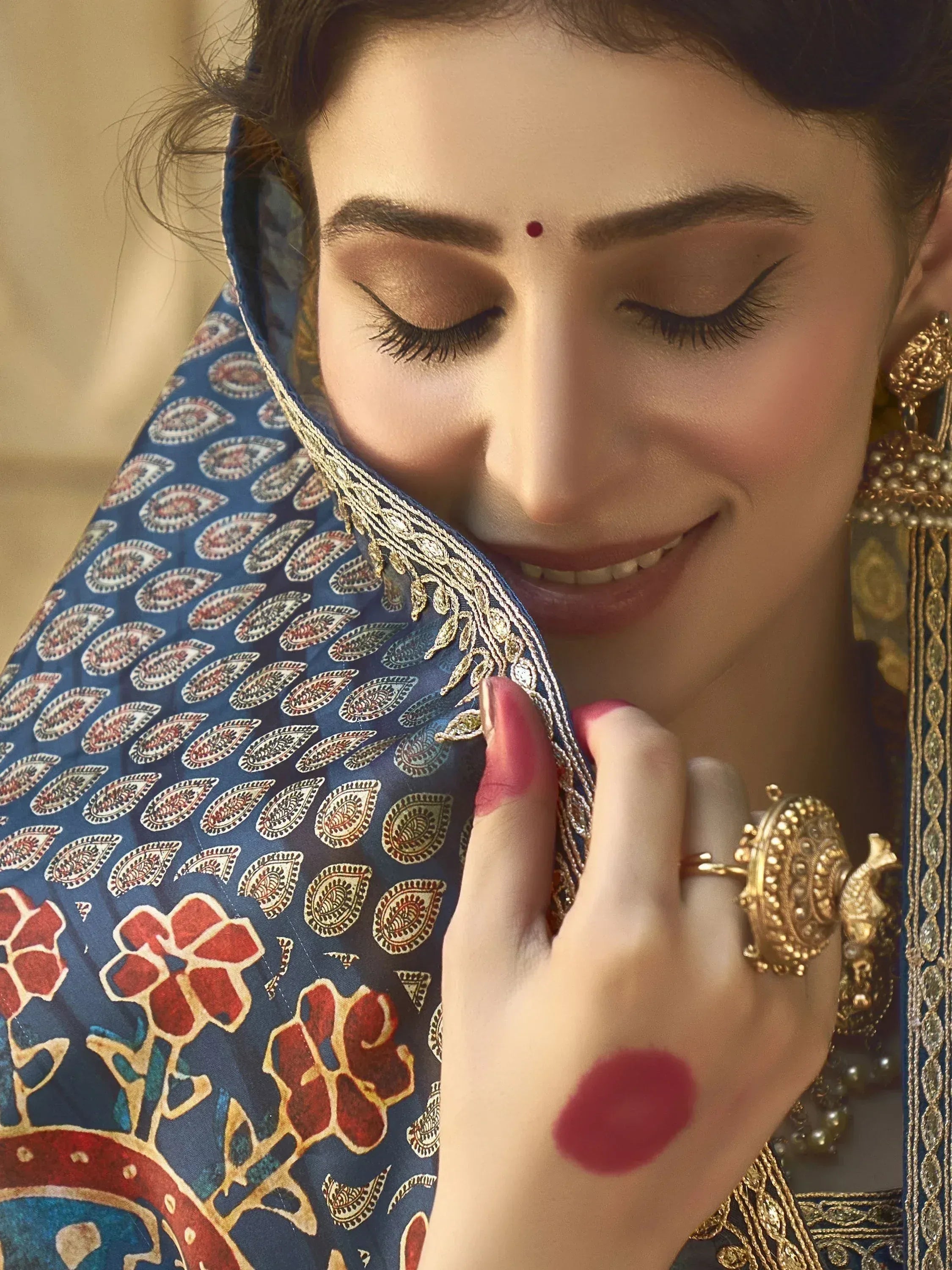 Woman in blue paisley ethnic saree with gold embroidery, traditional jewelry, and bindi, showcasing Indian fashion.
