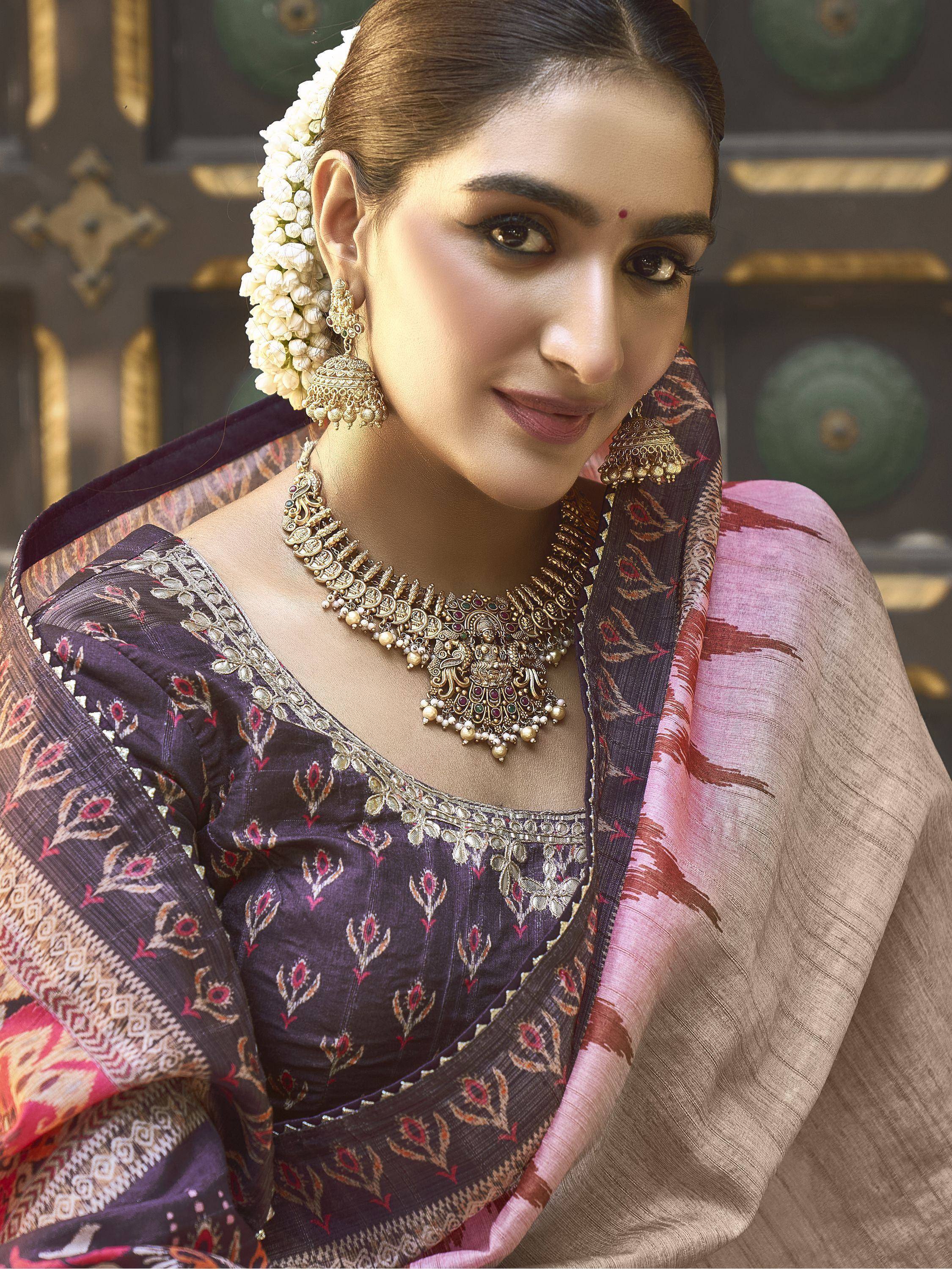 Woman in purple printed ethnic saree with gold jewelry and floral hair accessory