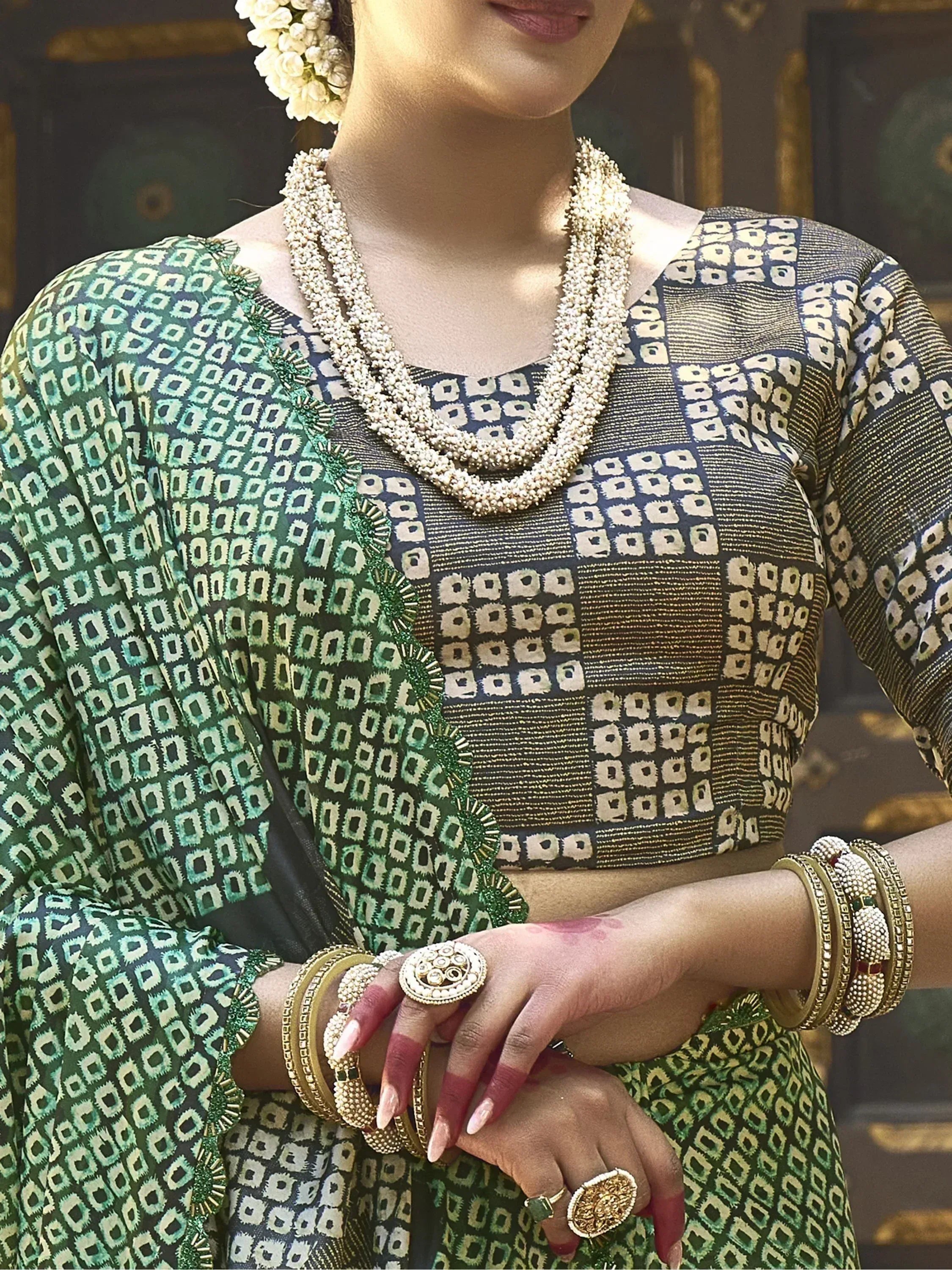 Green and gold patterned Indian saree with matching blouse, traditional jewelry, and floral hair accessory
