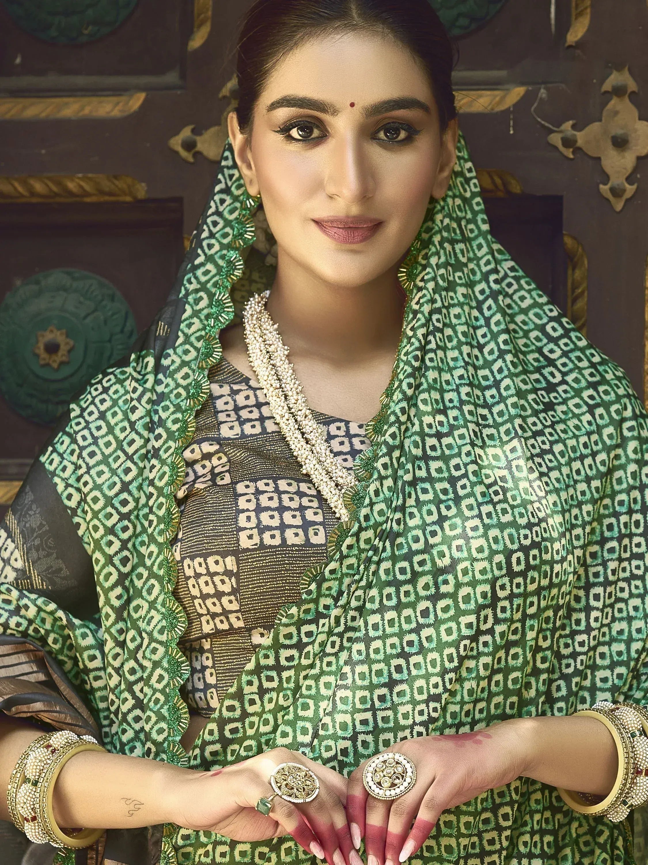 Woman in green patterned saree with gold jewelry, traditional Indian ethnic wear