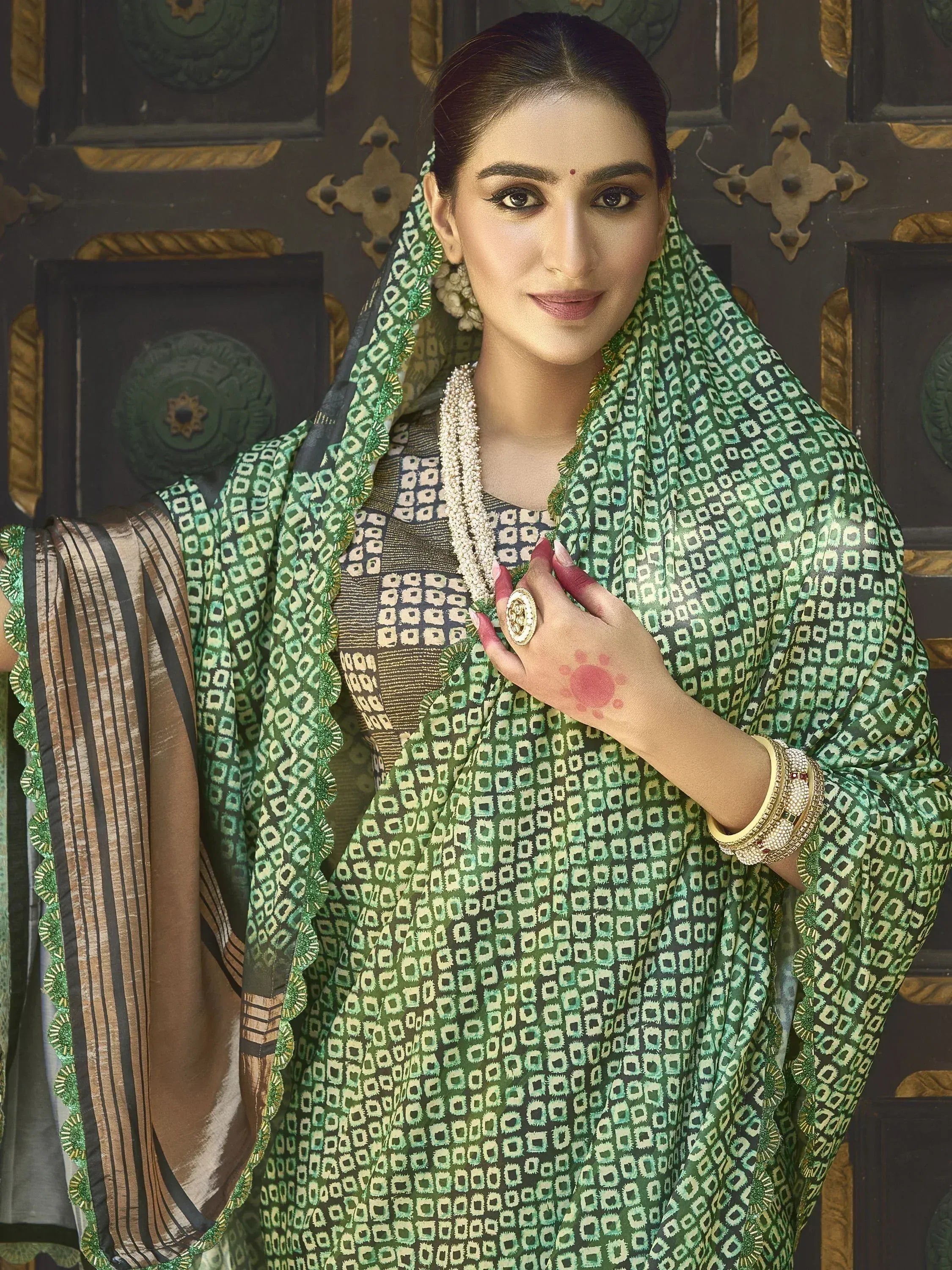 Woman in green patterned Indian ethnic wear with dupatta, traditional jewelry, and henna hand design