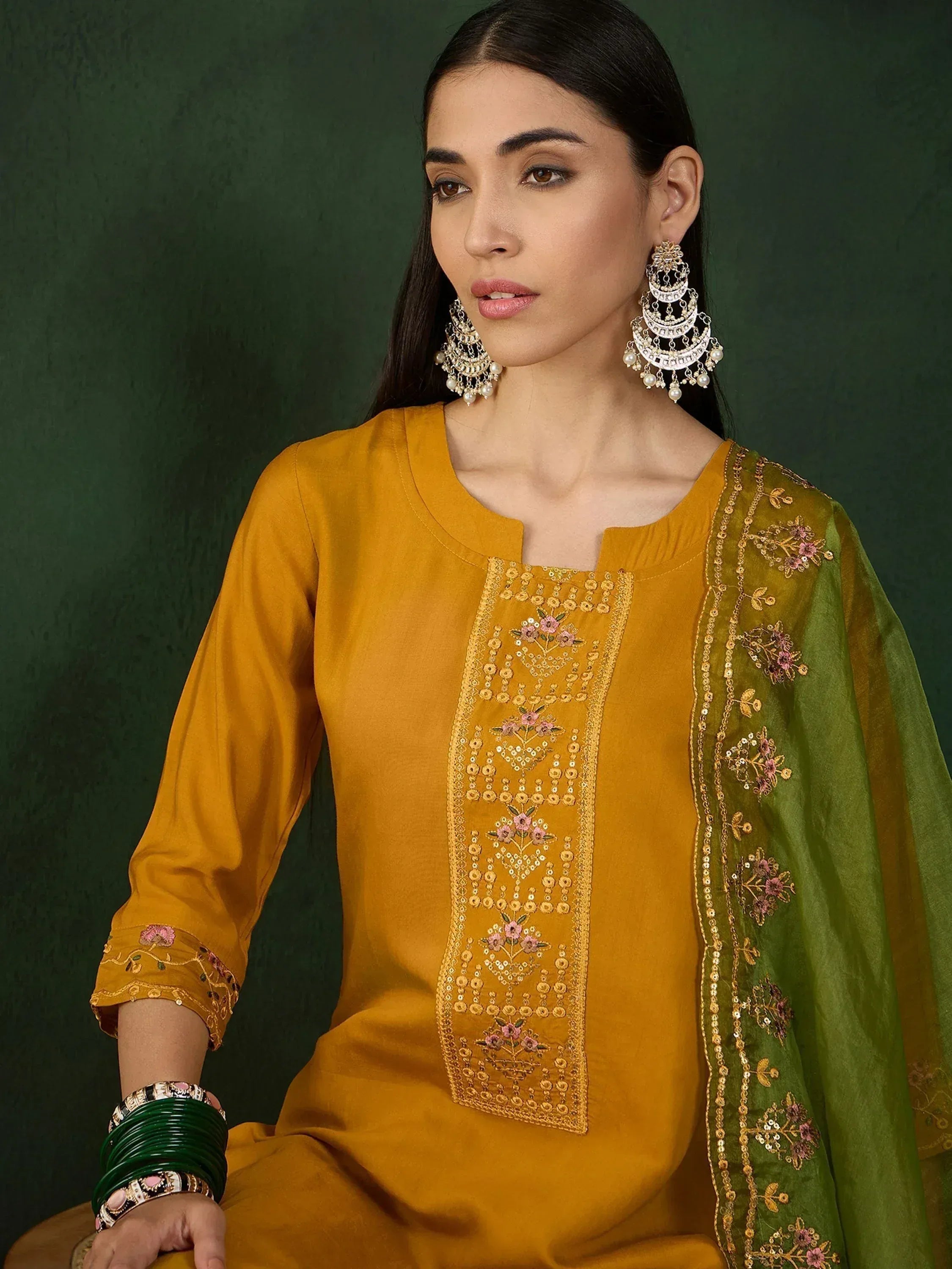 Mustard yellow embroidered salwar kameez with green dupatta, floral motifs, and traditional Indian jewelry