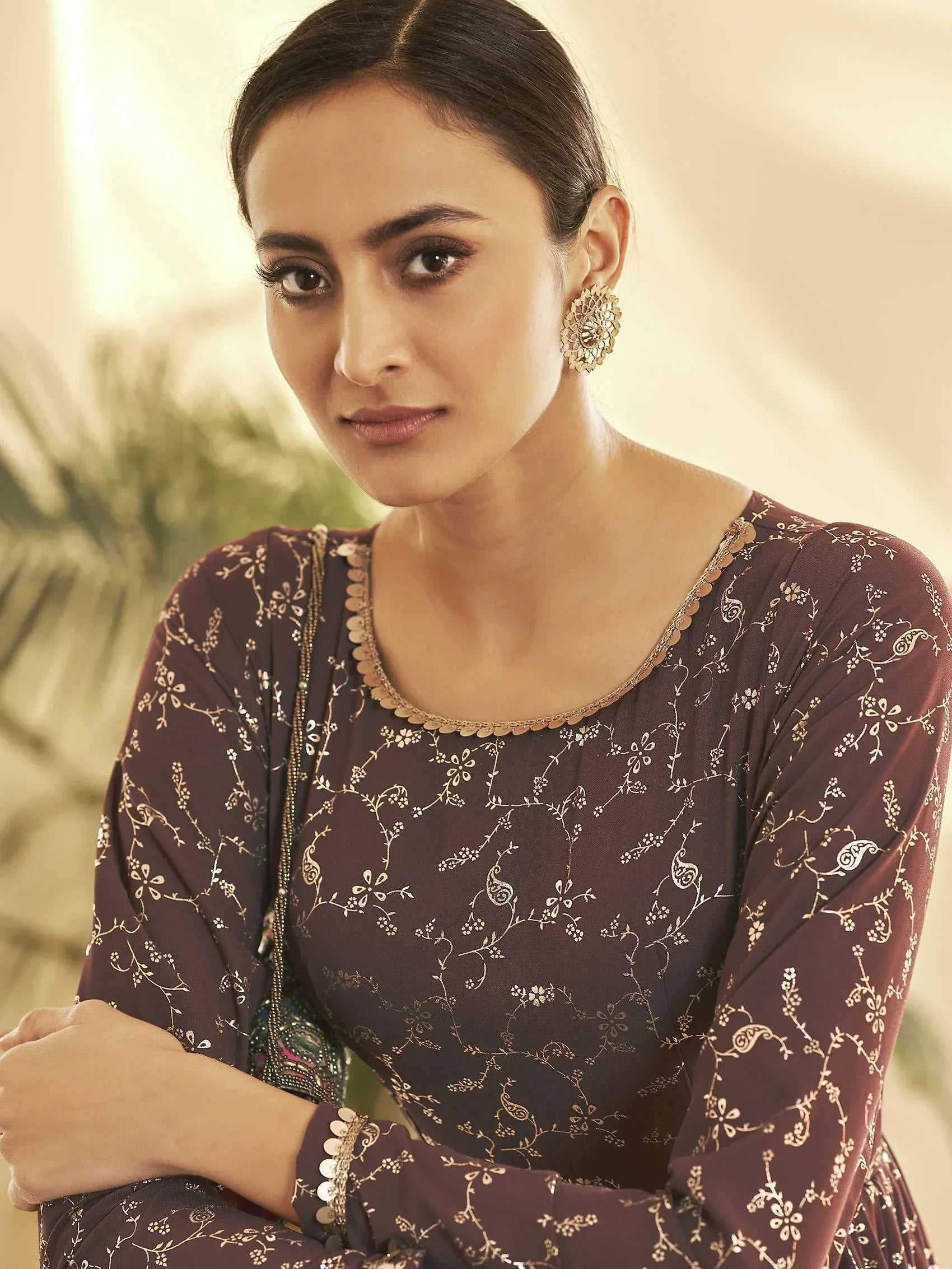 Woman in a maroon ethnic gown with gold floral print and statement earrings