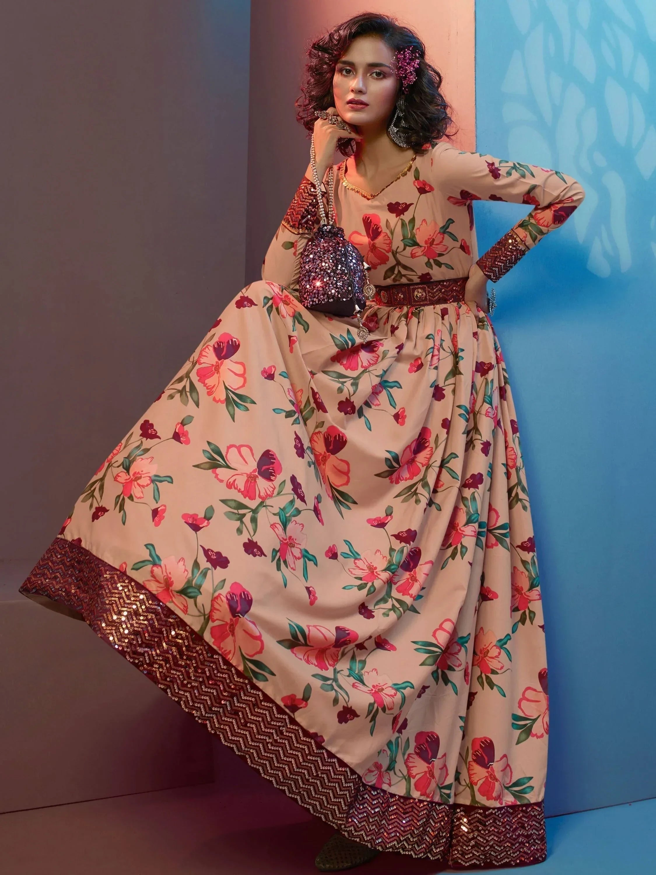 Woman wearing a long floral ethnic gown with sequin border, holding a sequin potli bag.