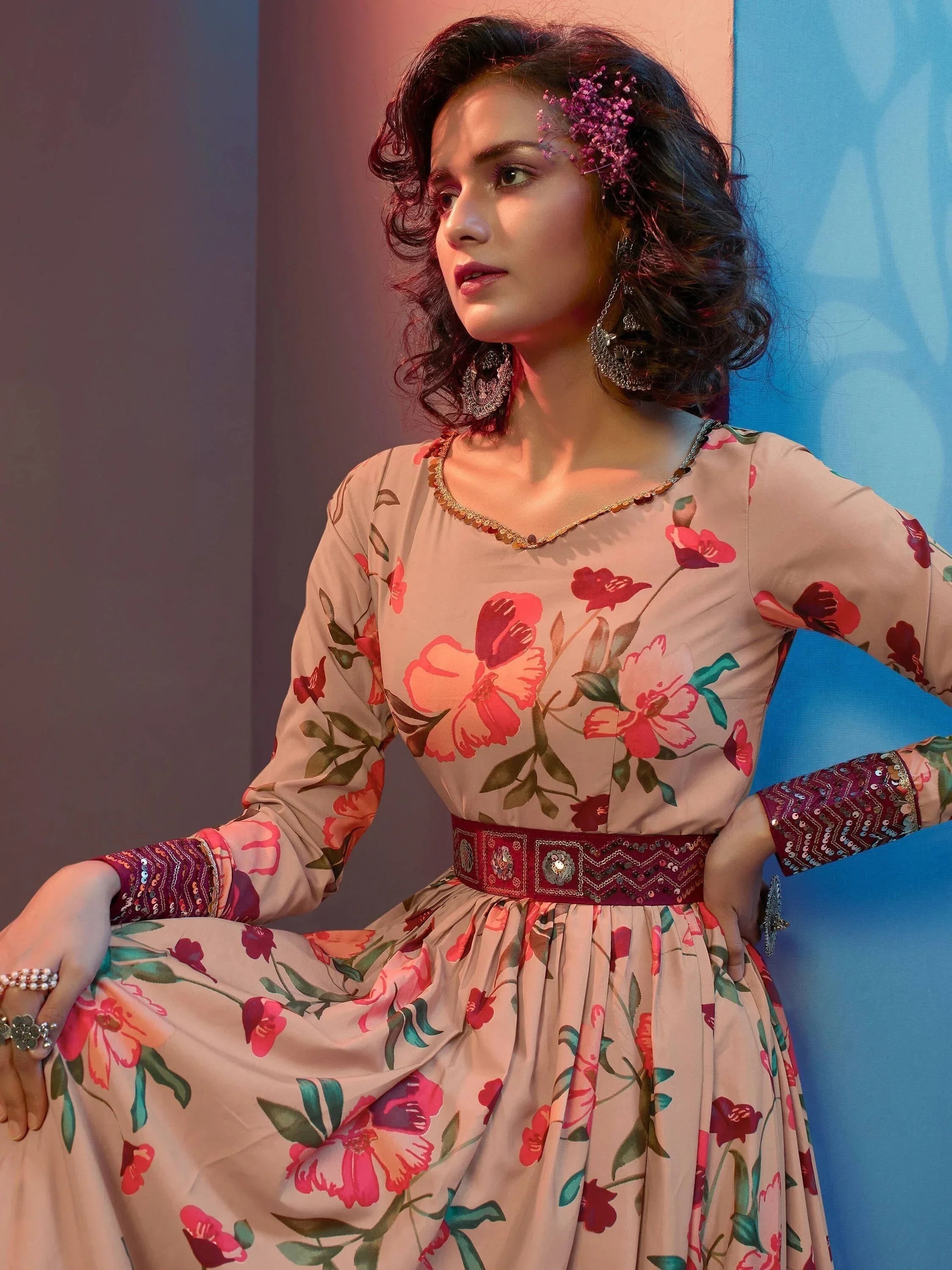 Woman in floral printed gown with pink and red flowers, embellished belt, and statement earrings