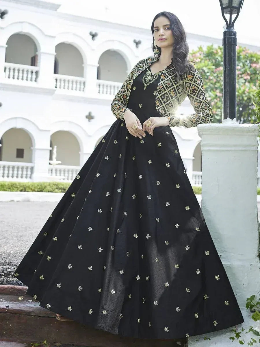 Woman in elegant black ethnic gown with gold embroidery and patterned jacket, outdoor setting