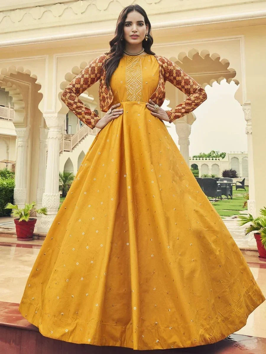 Woman in a mustard yellow embroidered Anarkali gown with patterned long sleeves, outdoors.