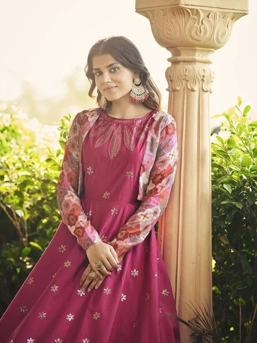 Woman in maroon embroidered ethnic gown with floral sleeves, standing beside carved pillar