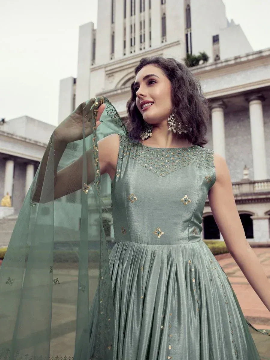 Woman in elegant sage green ethnic gown with gold embroidery and sheer dupatta, perfect for Indian occasions.