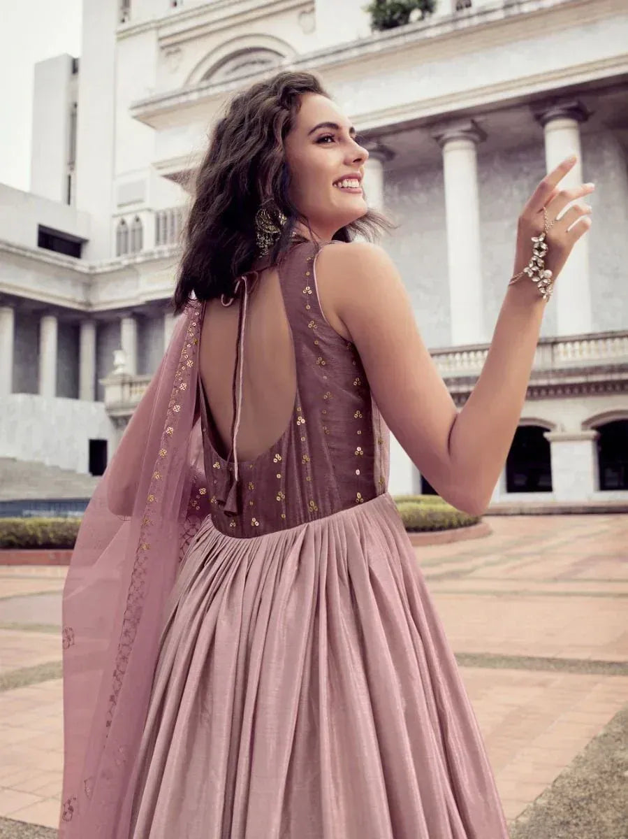 Woman wearing mauve ethnic gown with sequin details, standing outdoors near pillars.