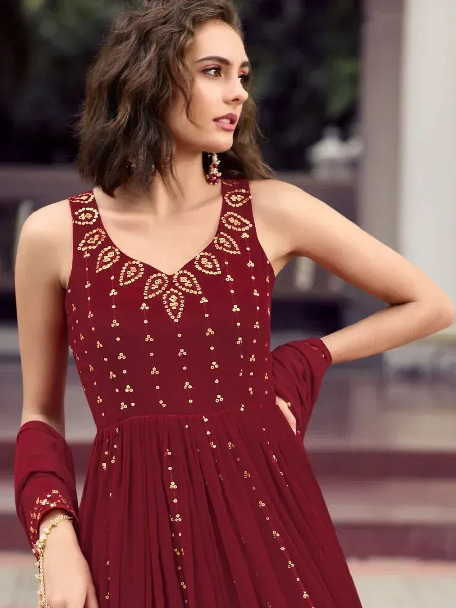 Woman wearing maroon sleeveless ethnic gown with gold embroidery, outdoor setting