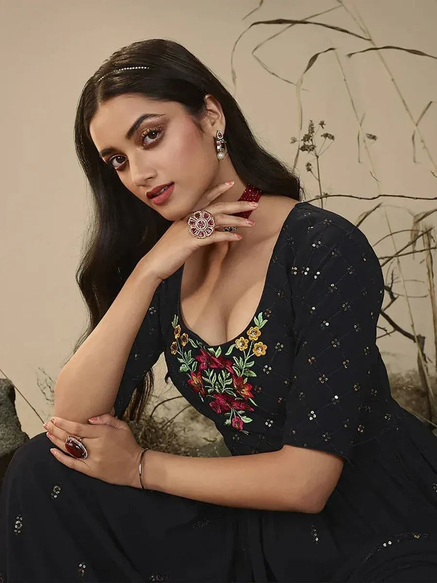 Woman wearing a black ethnic gown with floral embroidery, statement jewelry, and soft makeup
