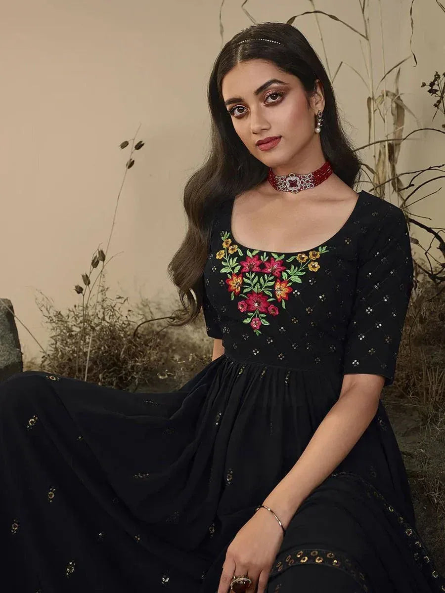 Woman in black embroidered ethnic gown with floral design, elegant jewelry, and natural background