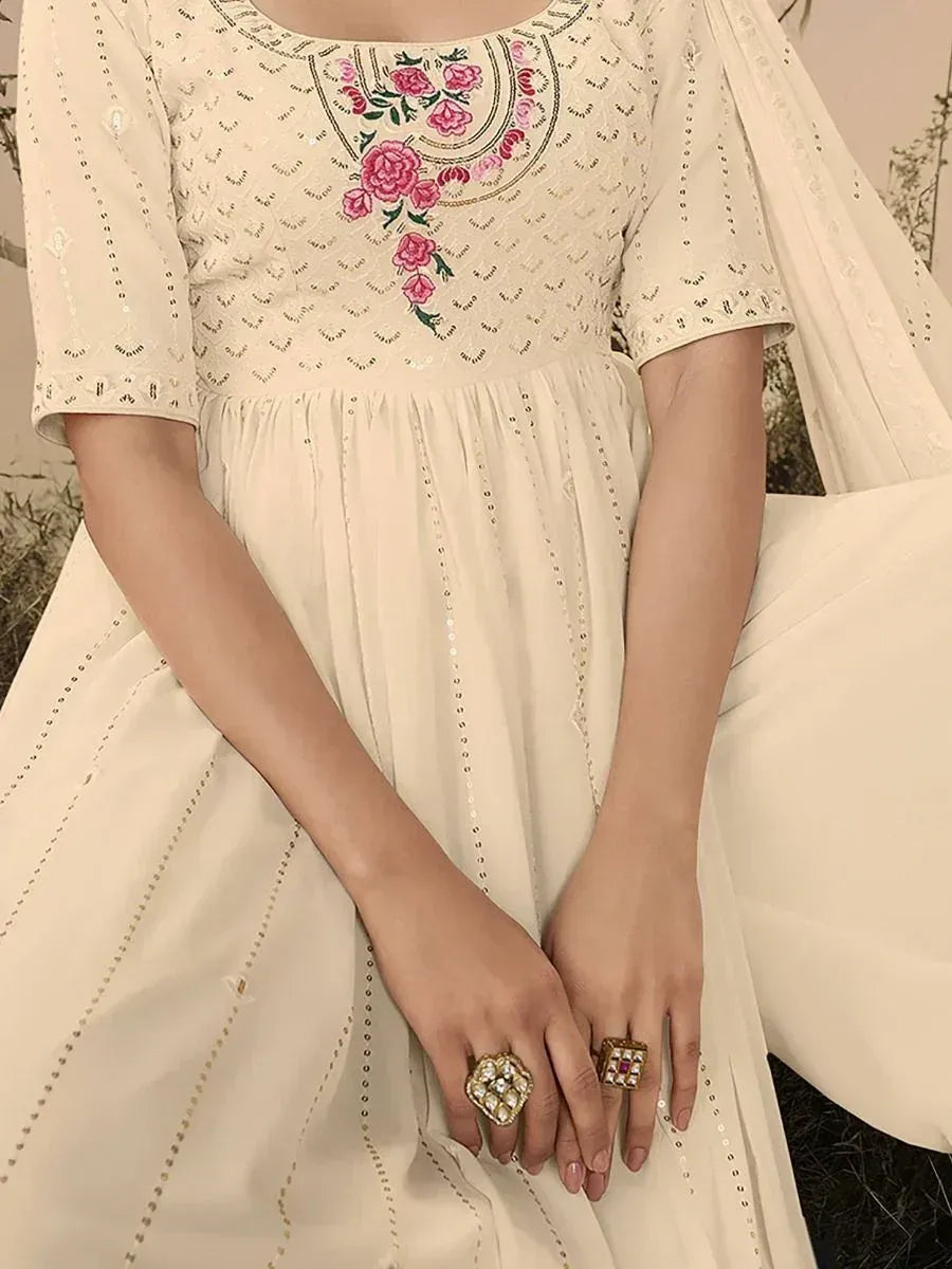 Beige ethnic gown with pink floral embroidery and sequin detailing, paired with statement rings