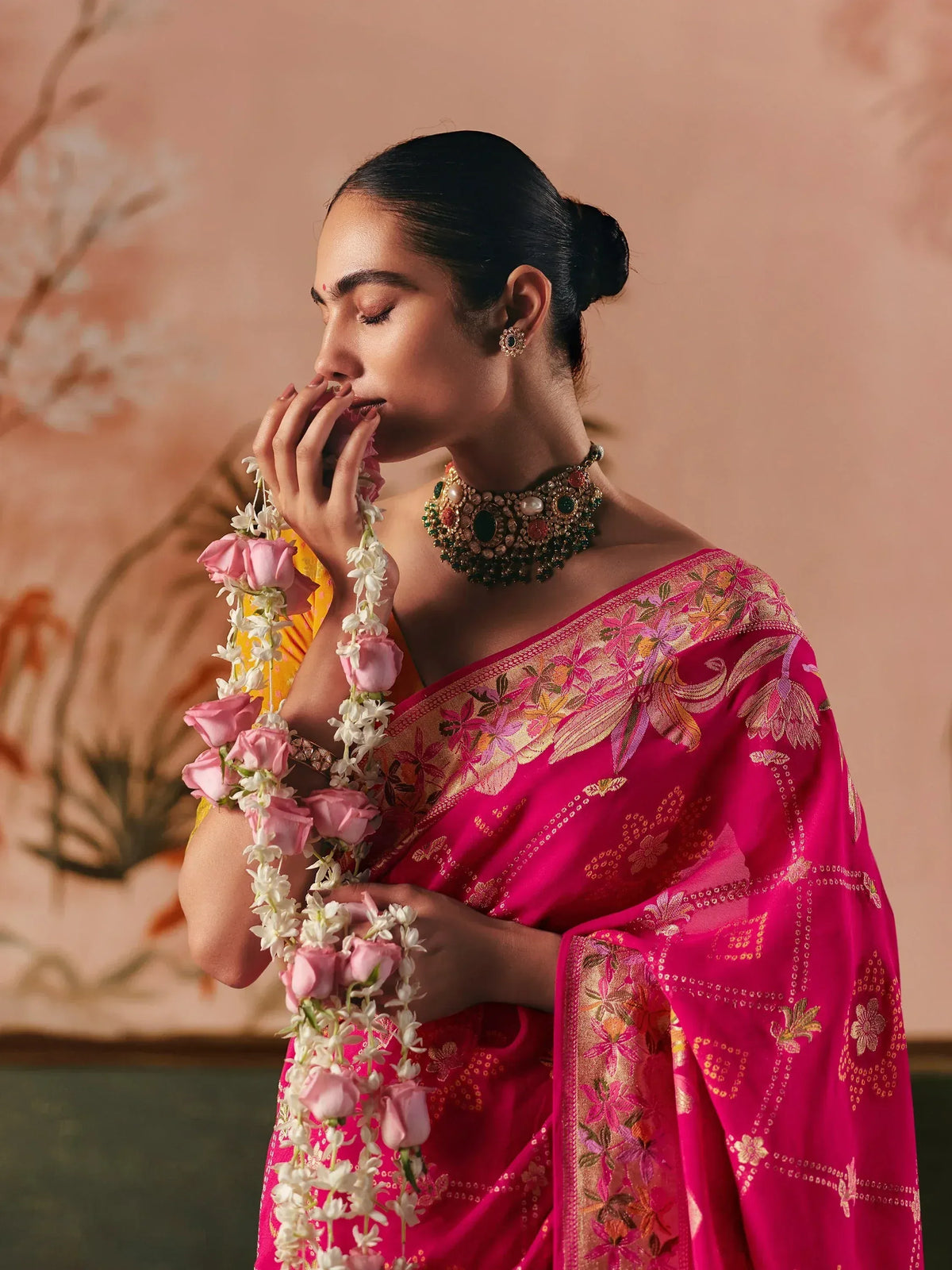 Woman in vibrant pink embroidered saree with floral garland and traditional jewelry