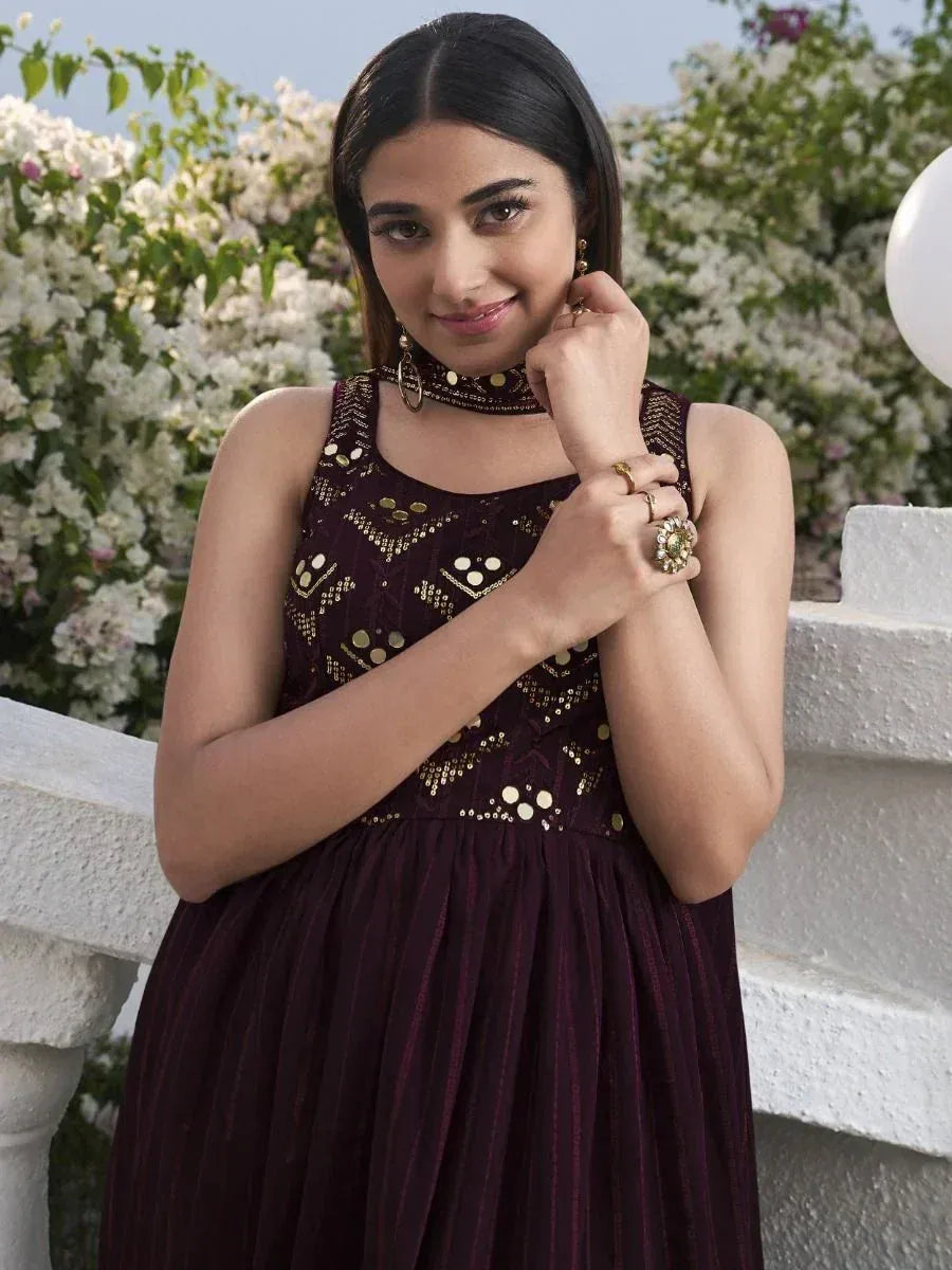 Woman in maroon ethnic gown with gold embellishments, floral backdrop, outdoor setting