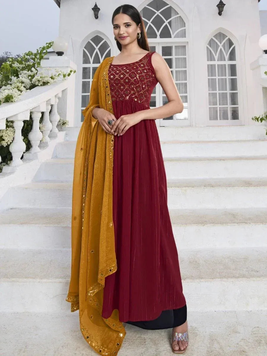 Woman wearing maroon embroidered ethnic gown with mustard dupatta, standing on stairs