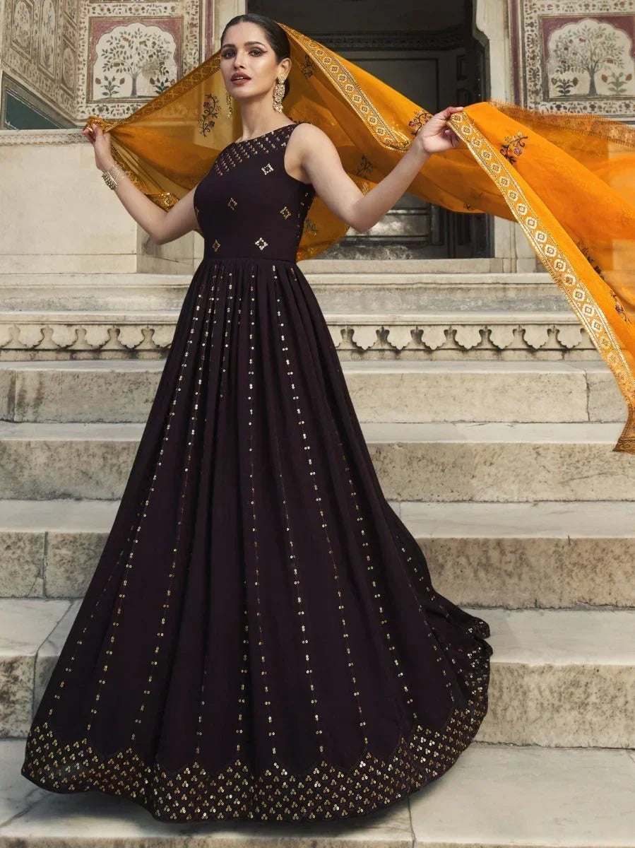 Woman in a black ethnic gown with gold mirror work and orange dupatta, standing on stone steps