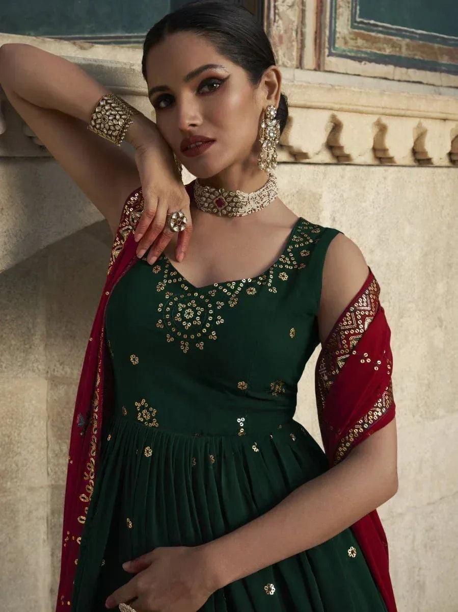 Emerald green ethnic gown with gold embroidery and red dupatta, styled with traditional jewelry for festive occasions.