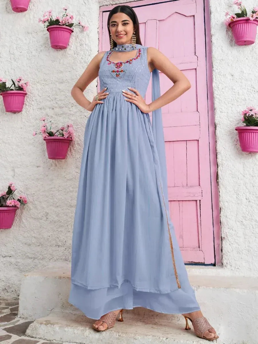 Woman in sleeveless lavender ethnic gown with floral embroidery, standing by pink door