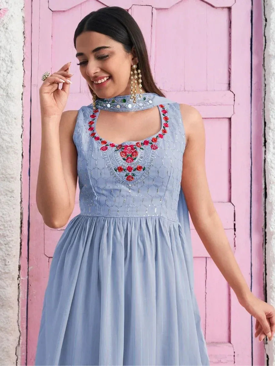 Woman wearing light blue ethnic gown with floral embroidery and mirror work, posing indoors