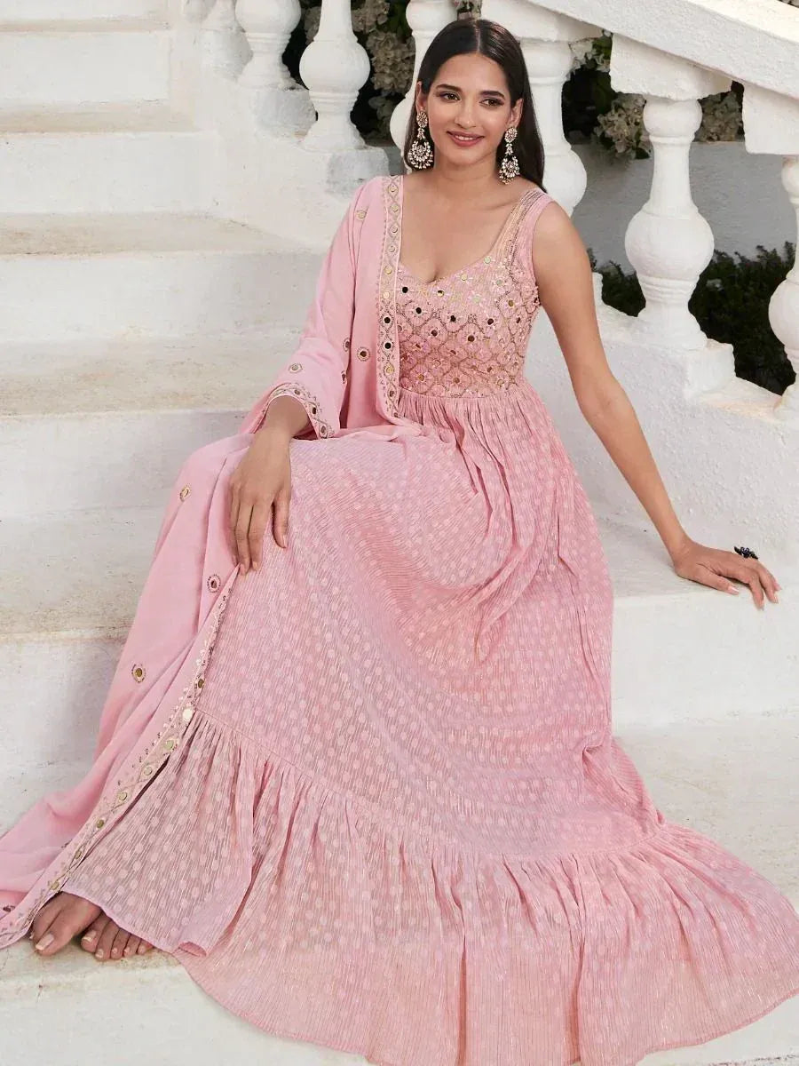 Woman in light pink embroidered ethnic gown with dupatta sitting on white stairs